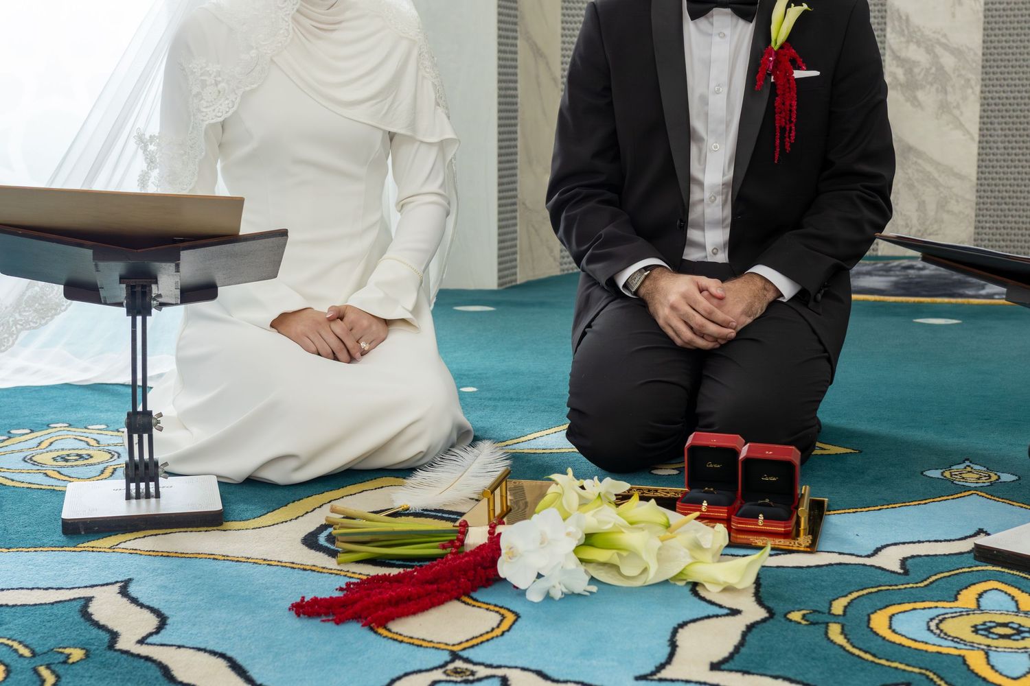 Muslim couple kneeling during traditional Islamic wedding ceremony with rings and flowers on ornate carpet.