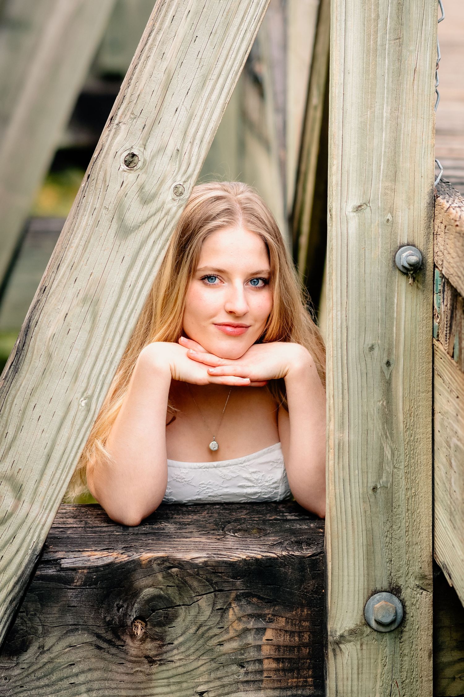 Portrait of someone leaning on wooden beams in casual attire with soft natural lighting.
