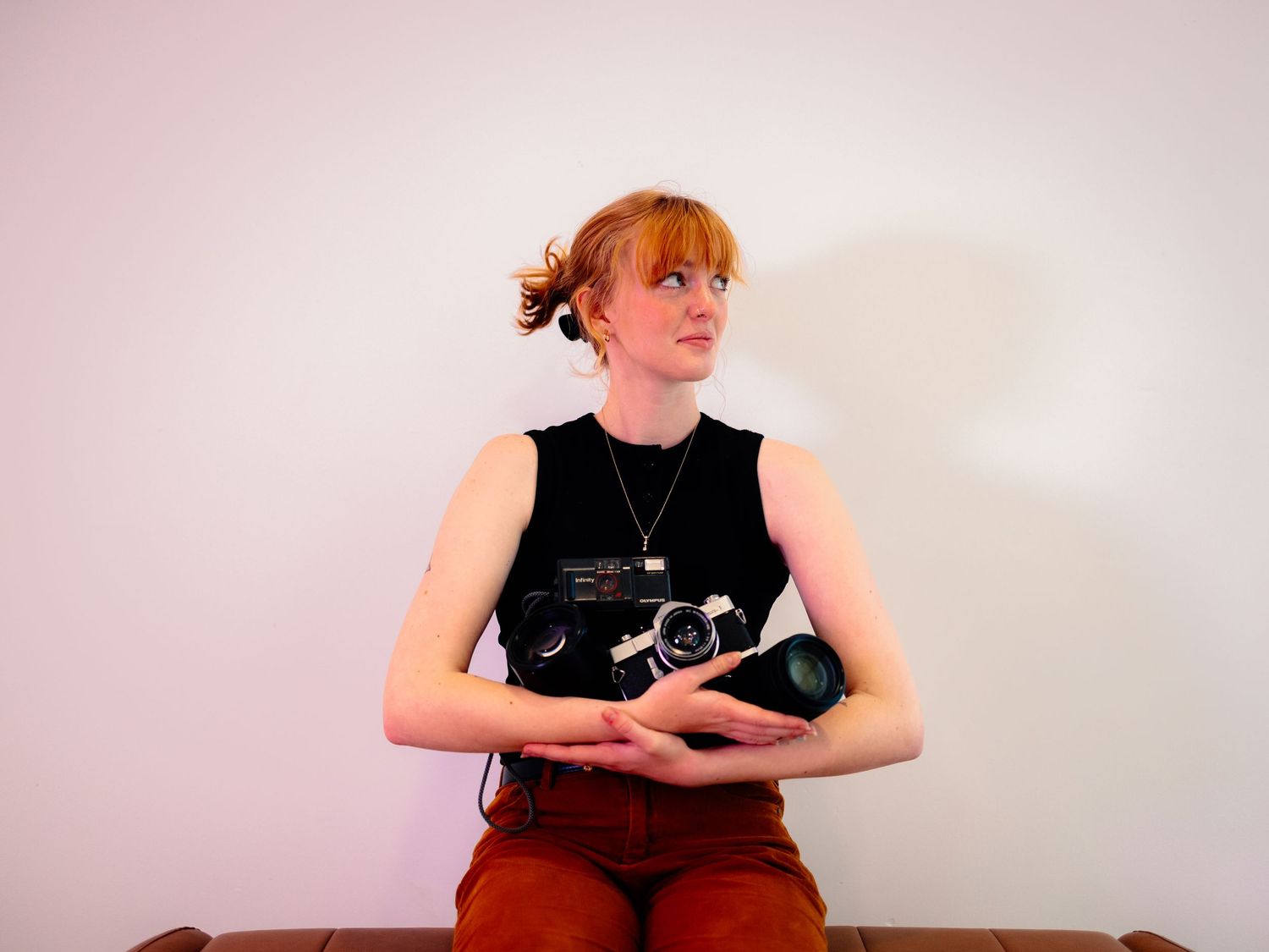 Woman in sleeveless black top seated against white background.
