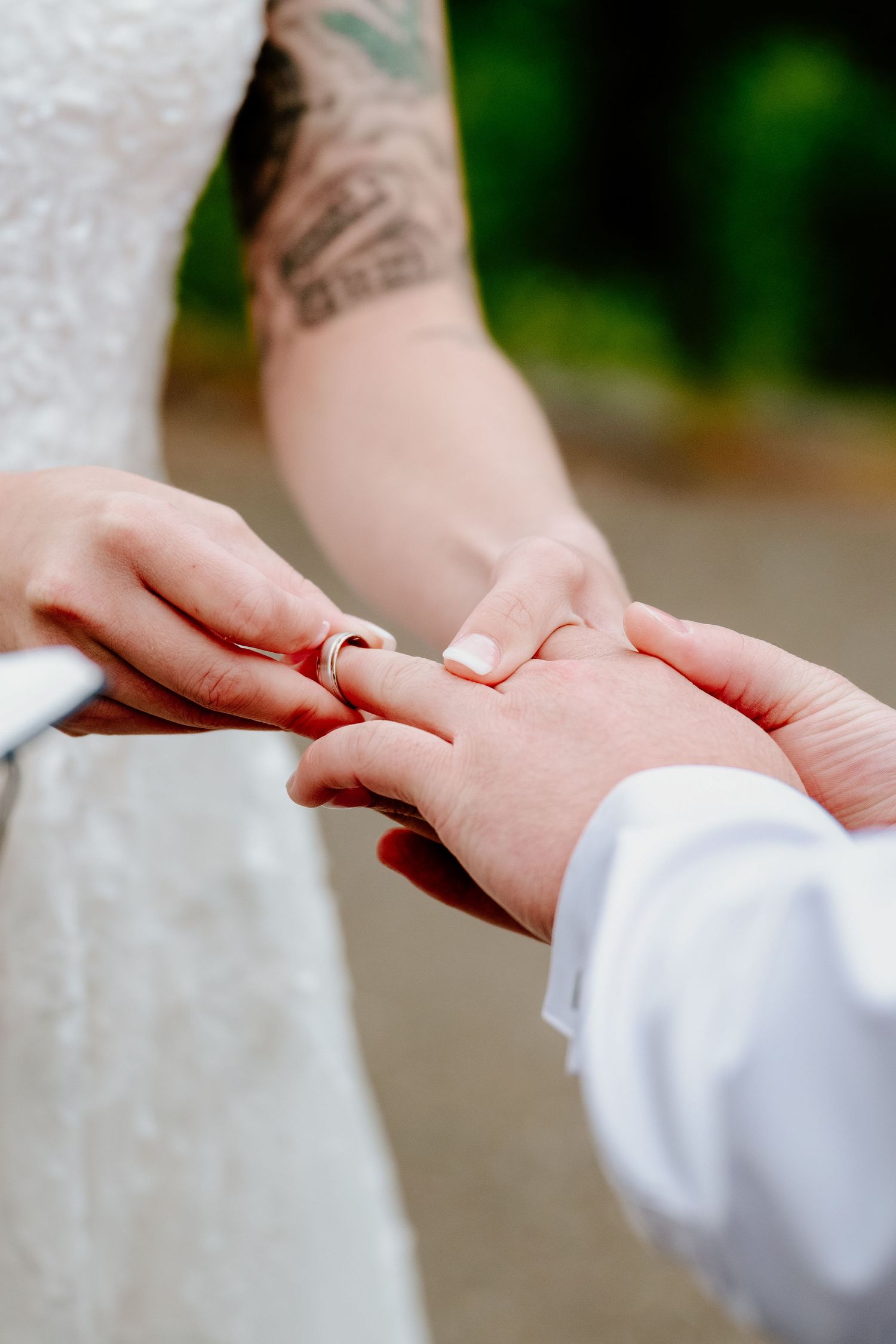 Close-up of hands exchanging wedding rings during ceremony with visible tattoo detail.