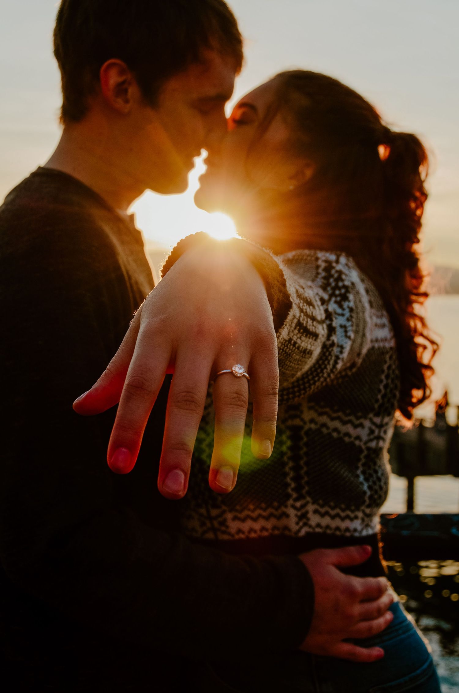 A romantic sunset engagement photo showing a ring on display as a couple shares an intimate moment.