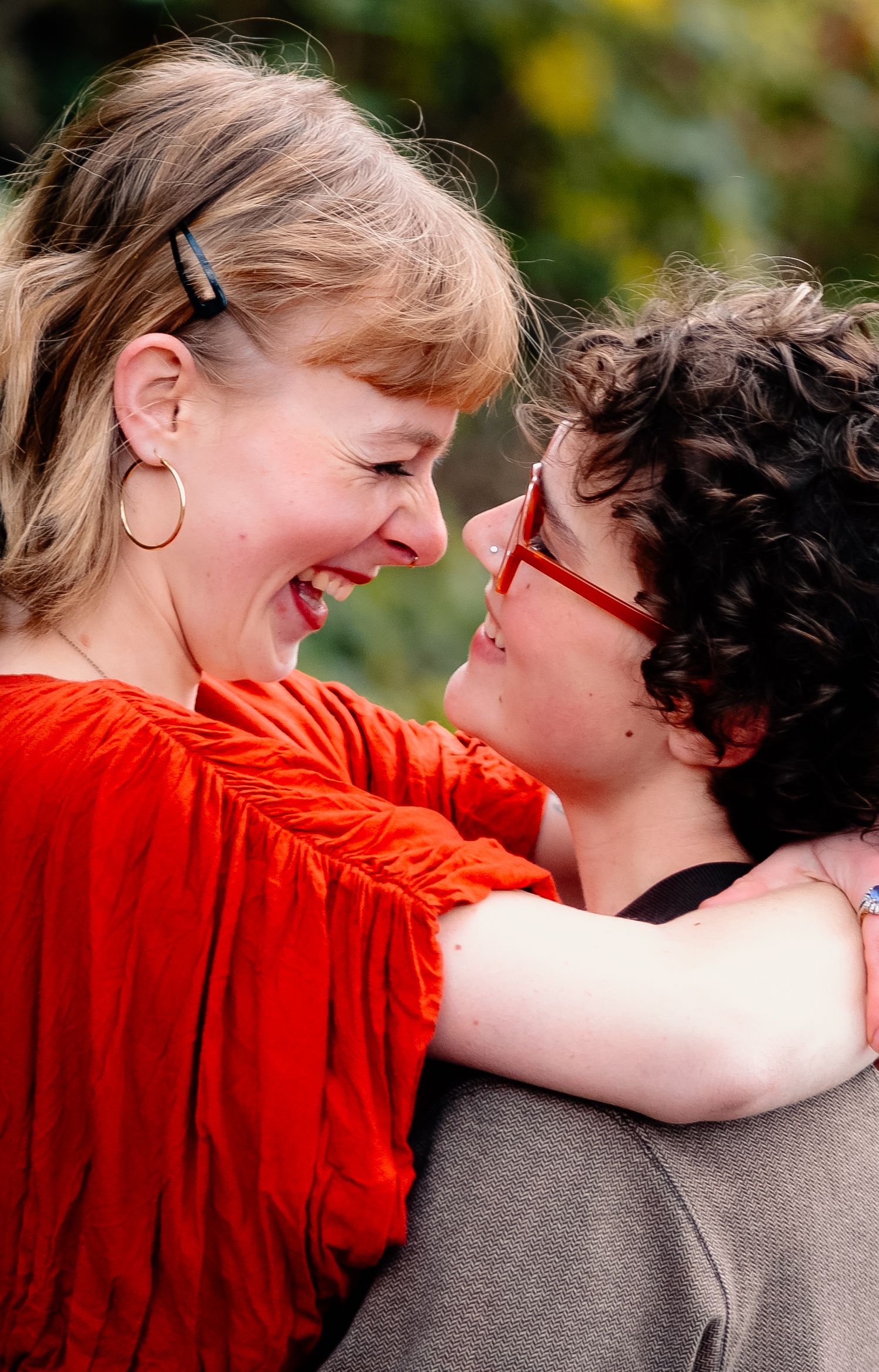 A couple embraces and shares a tender moment outdoors in warm sunlight, wearing red and gray clothing.