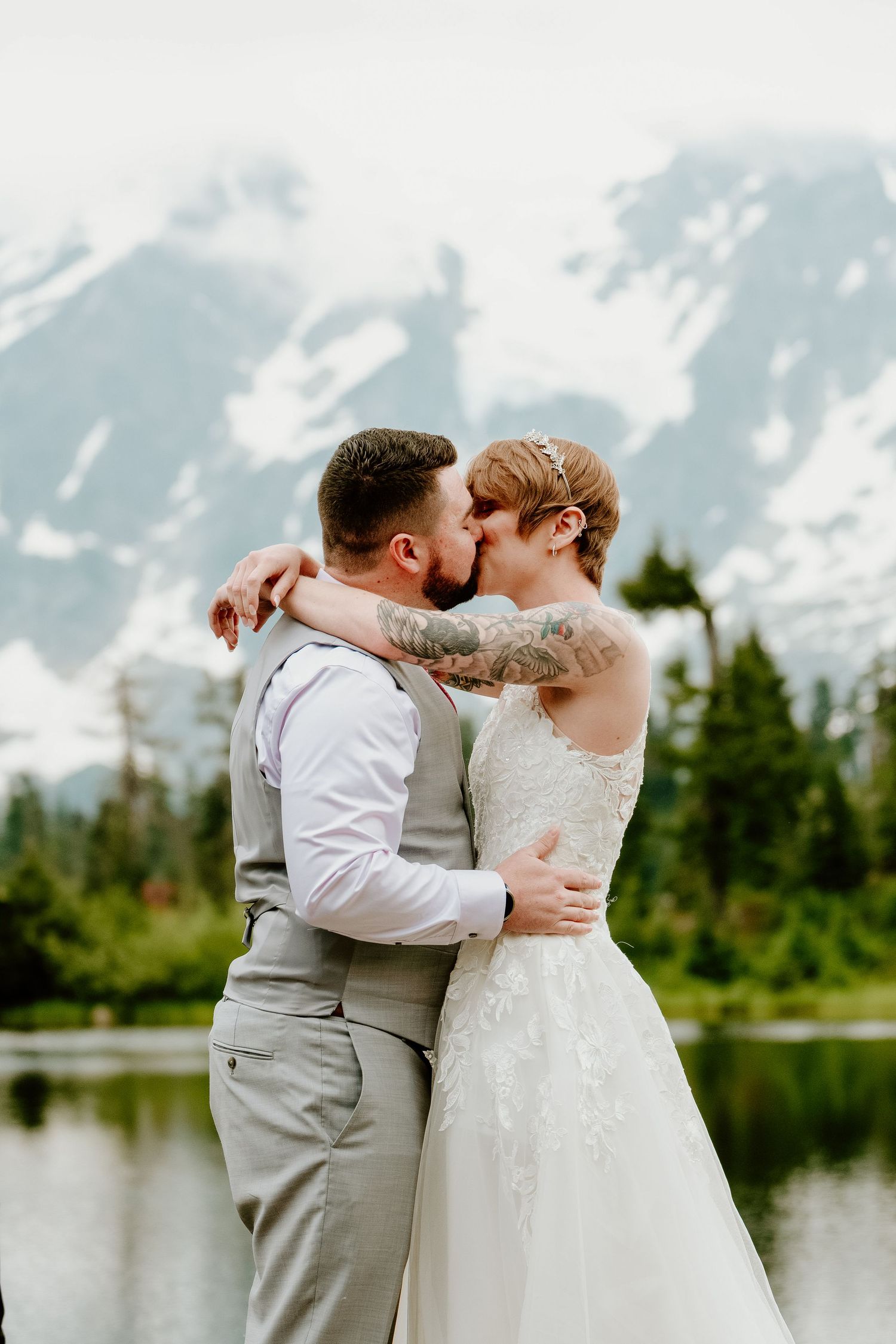 Romantic wedding portrait against snowy mountain landscape with lake and forest backdrop.