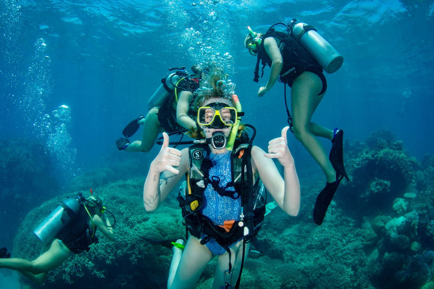 Scuba divers explore vibrant coral reefs in crystal clear blue tropical waters during an underwater diving excursion.