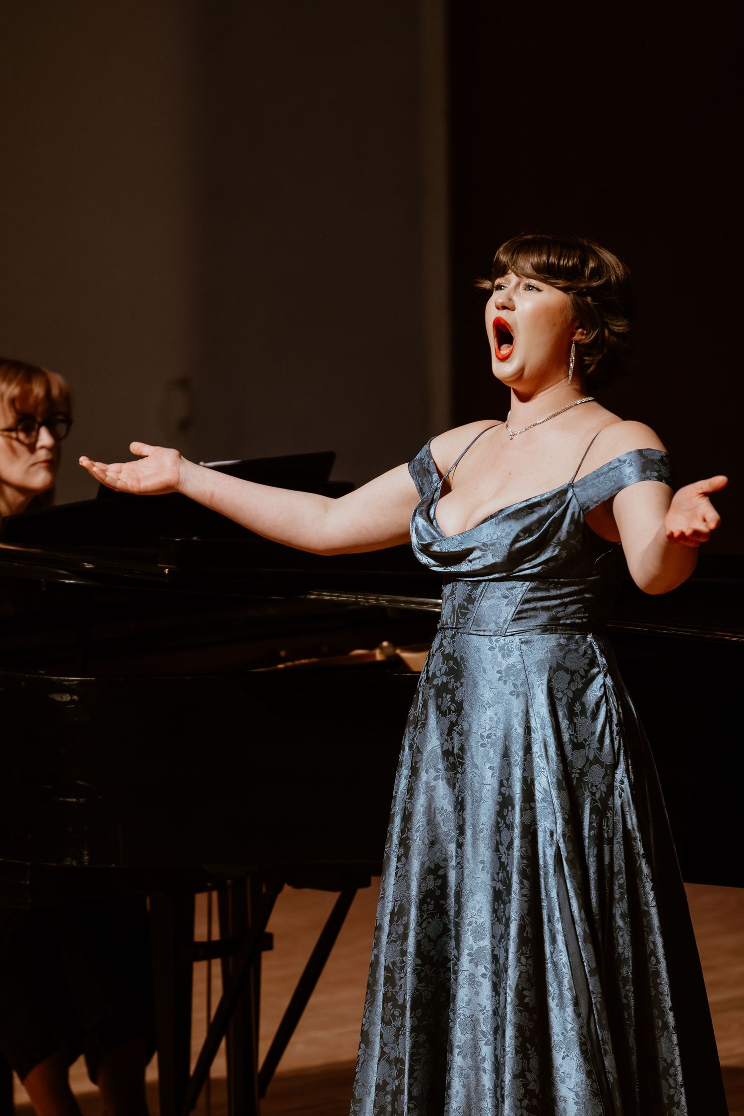 Opera singer performing passionately in blue evening gown with pianist.