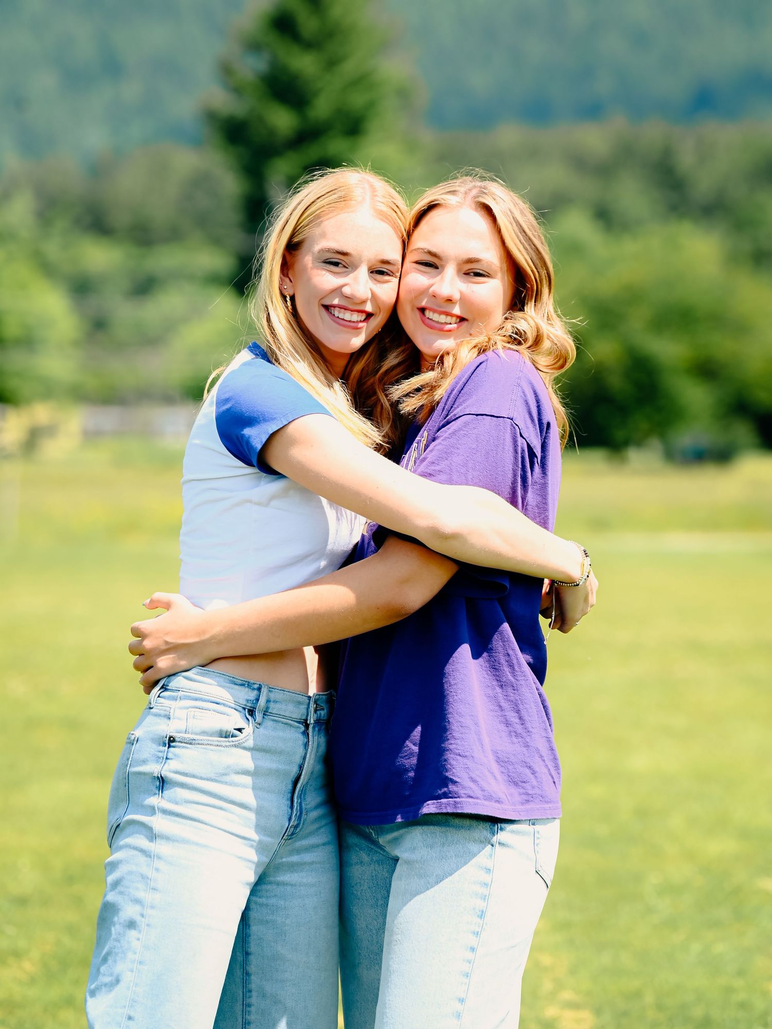 Friends hugging and laughing together in casual outfits against a scenic mountain backdrop.