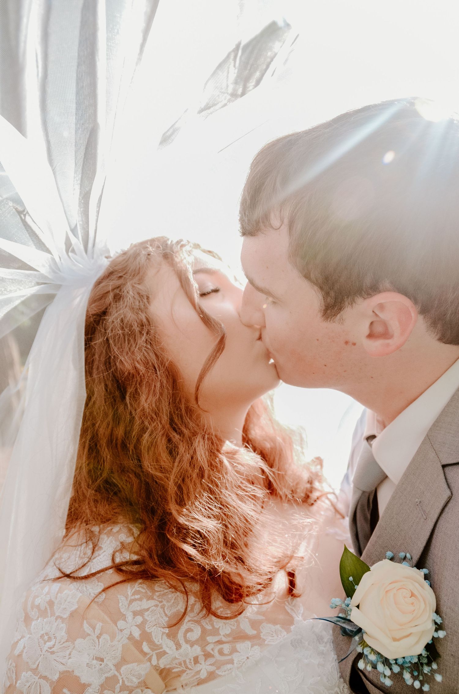 Intimate wedding moment captured in soft light with flowing veil and white rose boutonniere.