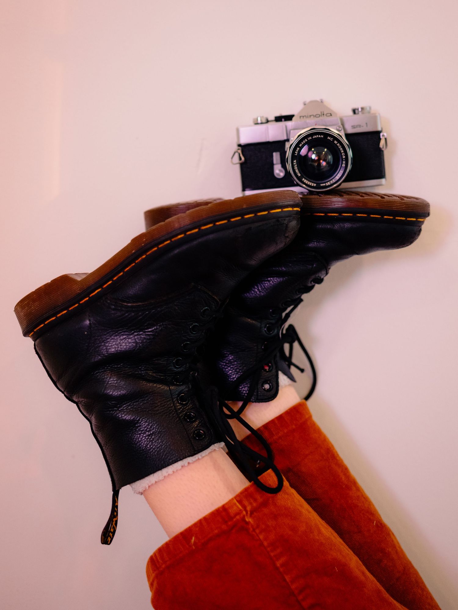 Black leather boots displayed on orange fabric against pink background.