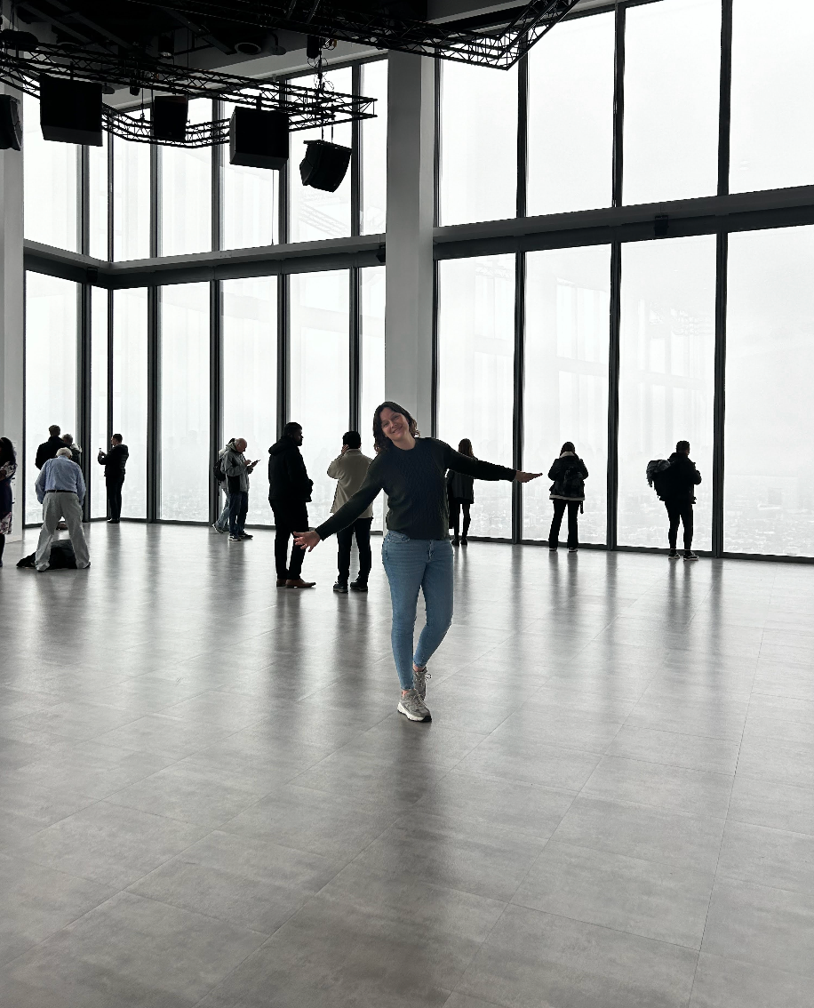 Silhouetted visitors observe city views from a modern observation deck while someone jumps joyfully in the foreground.
