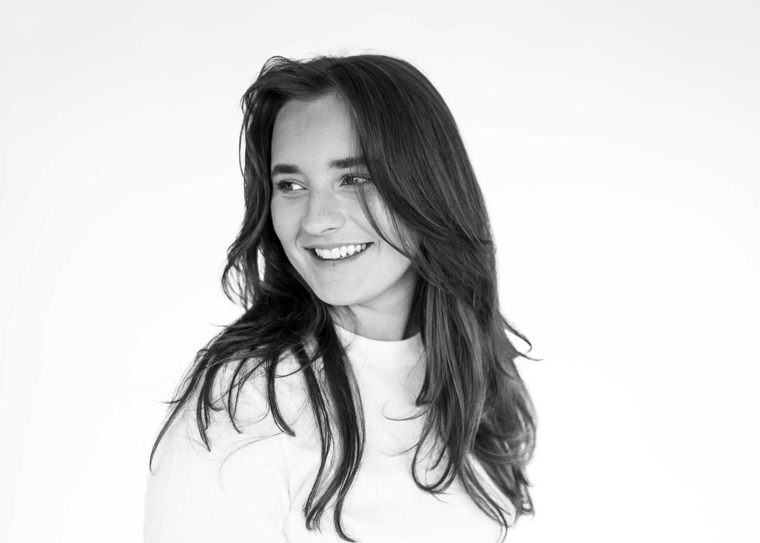 Black and white portrait of a smiling young woman with long dark hair wearing a white top.