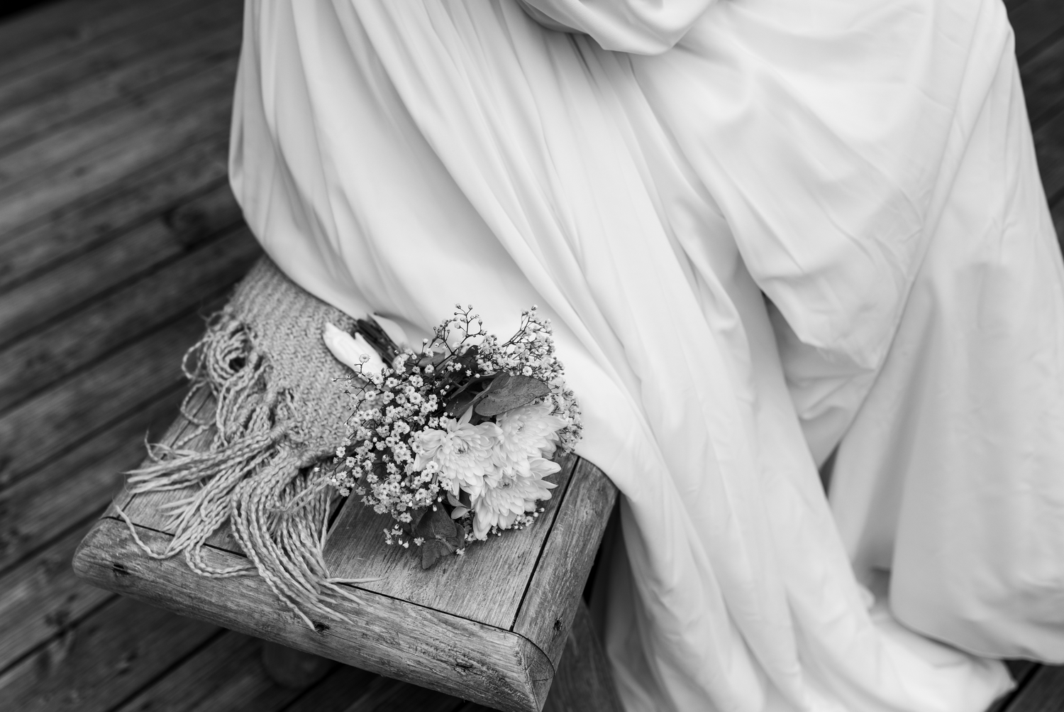 A delicate flower bouquet wrapped in lace rests on an ornate wooden box in black and white.
