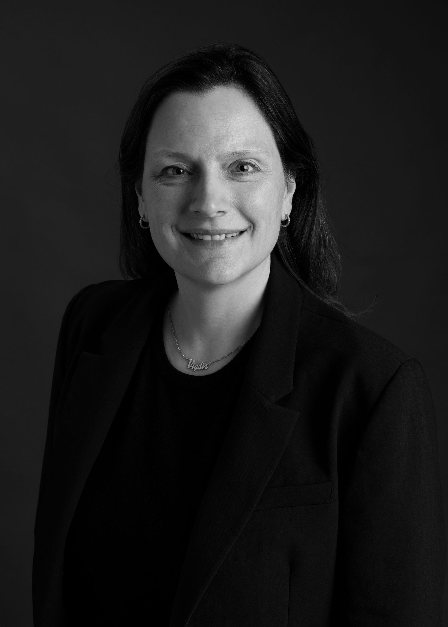 Professional headshot of person in black blazer against dark background.