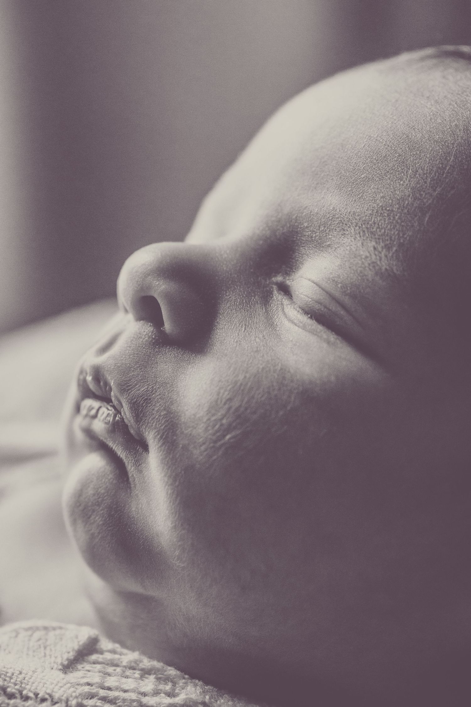 A close-up black and white portrait of a sleeping baby's peaceful face in soft focus.