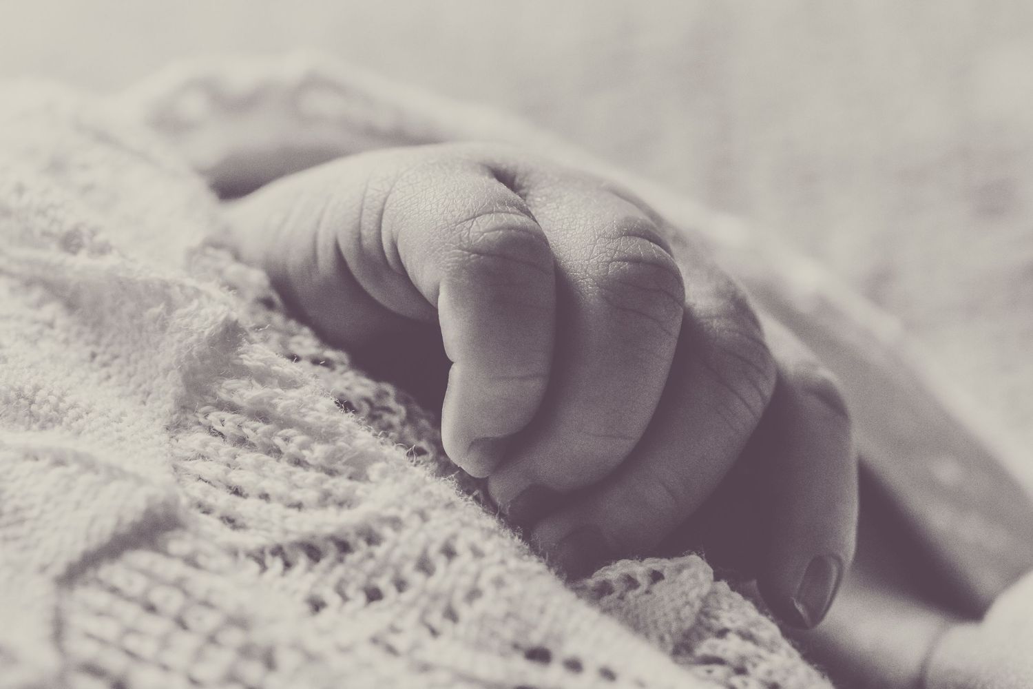 Delicate baby hand resting on knitted fabric in monochrome.