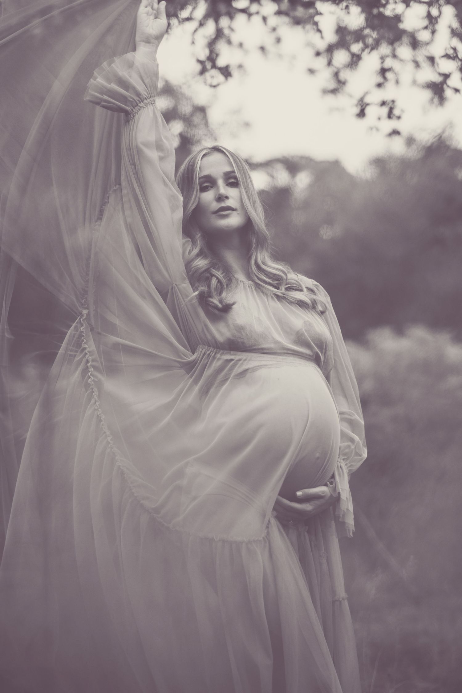 Black and white maternity portrait with flowing dress and ethereal lighting.