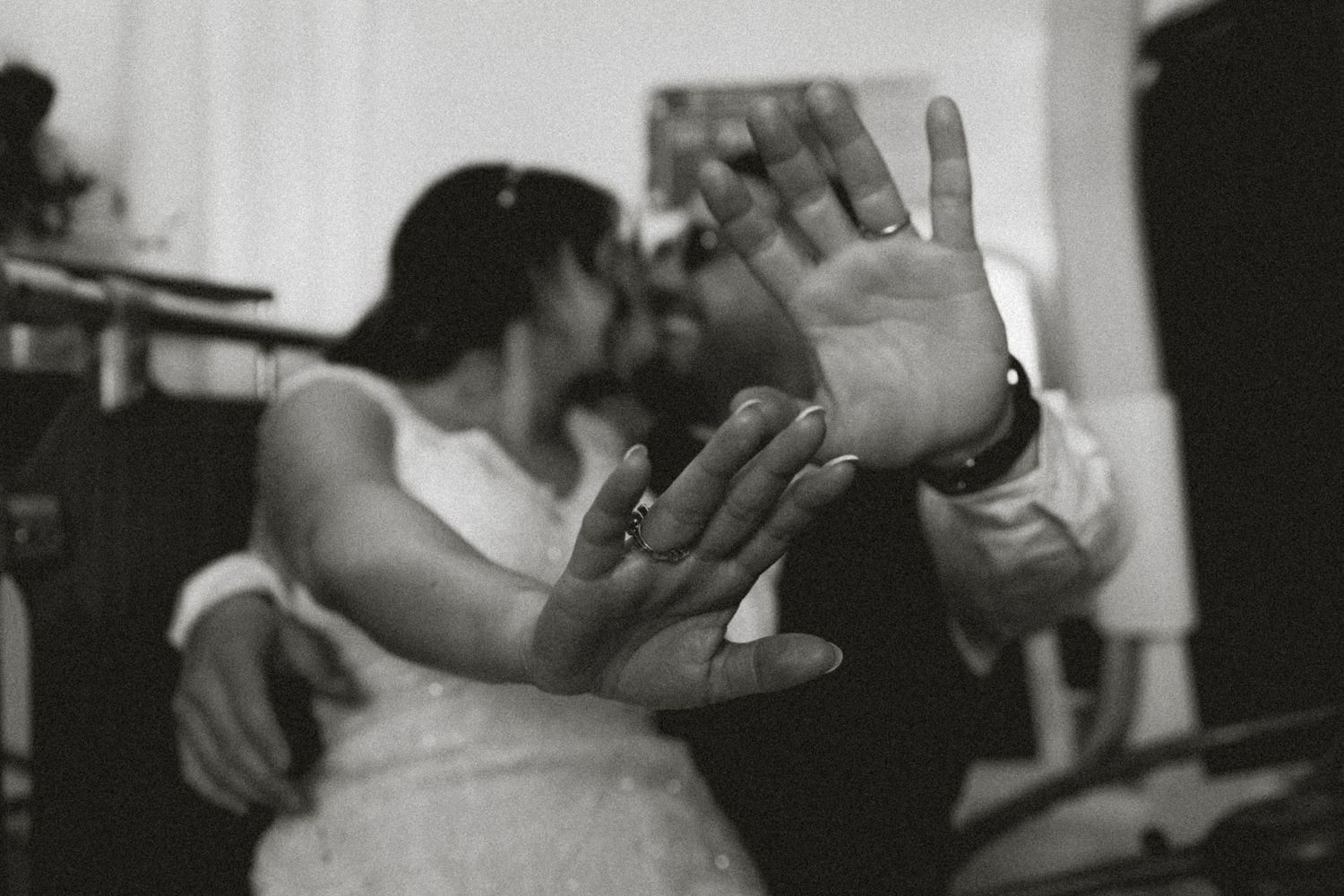 Black and white wedding photo of couple kissing while showing off their wedding rings to the camera.