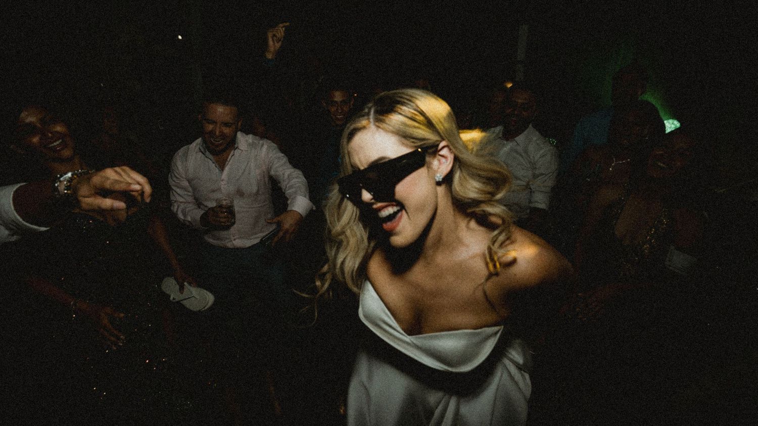 Briden in white dress wearing black masquerade mask dancing at a lively evening party celebration.
