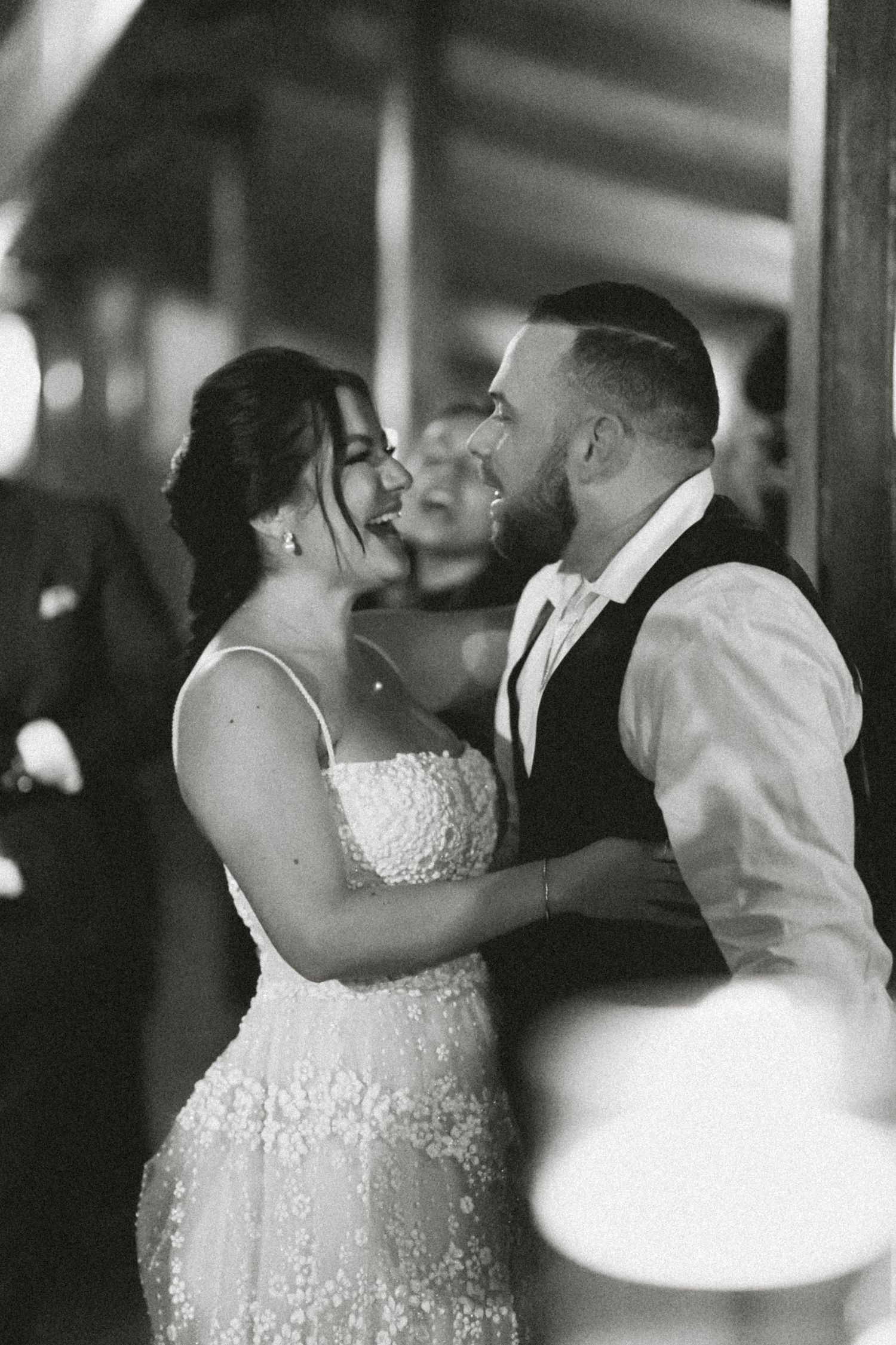 Black and white photo of a bride and groom sharing their first dance, smiling intimately at each other during wedding reception.