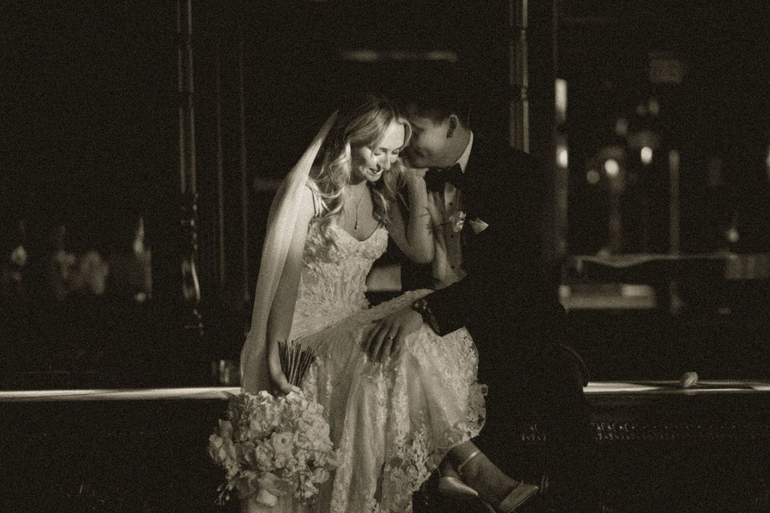 Black and white photo of a bride and groom sharing an intimate moment, sitting together at night.