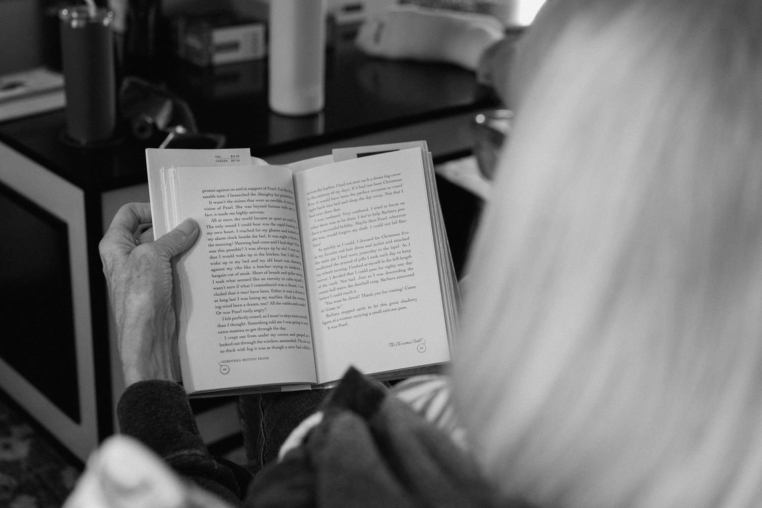 Blonde woman reading an open book indoors, black and white photography.