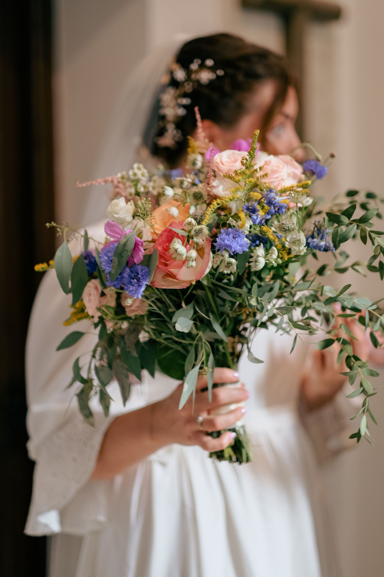 A delicate floral arrangement with pink and purple blooms is held against a white dress in natural light.