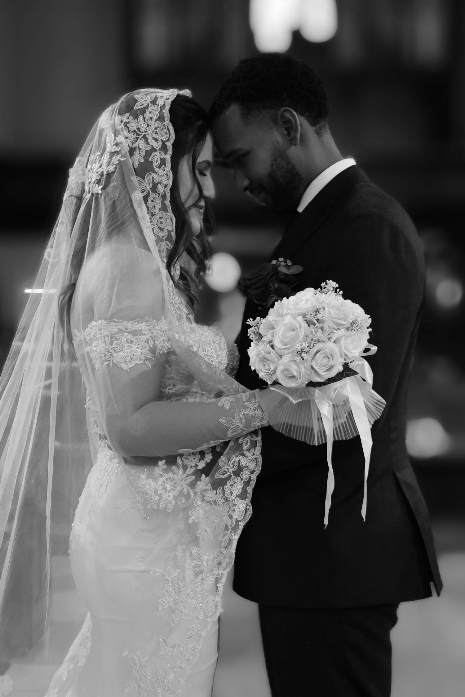 A tender black and white wedding photograph showing a couple during an intimate moment with a white rose bouquet.