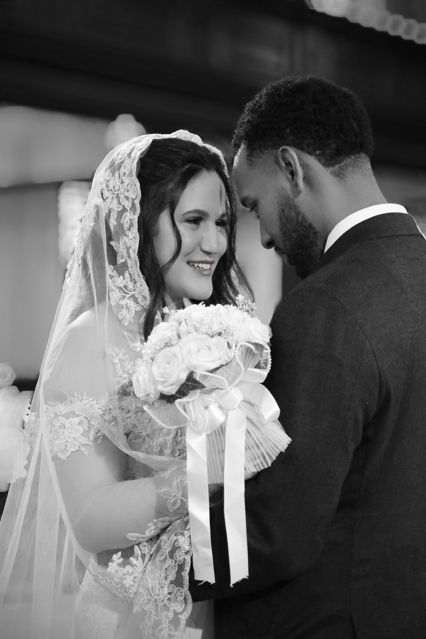 Black and white wedding photo of a happy couple sharing an intimate moment as the bride holds a white rose bouquet.