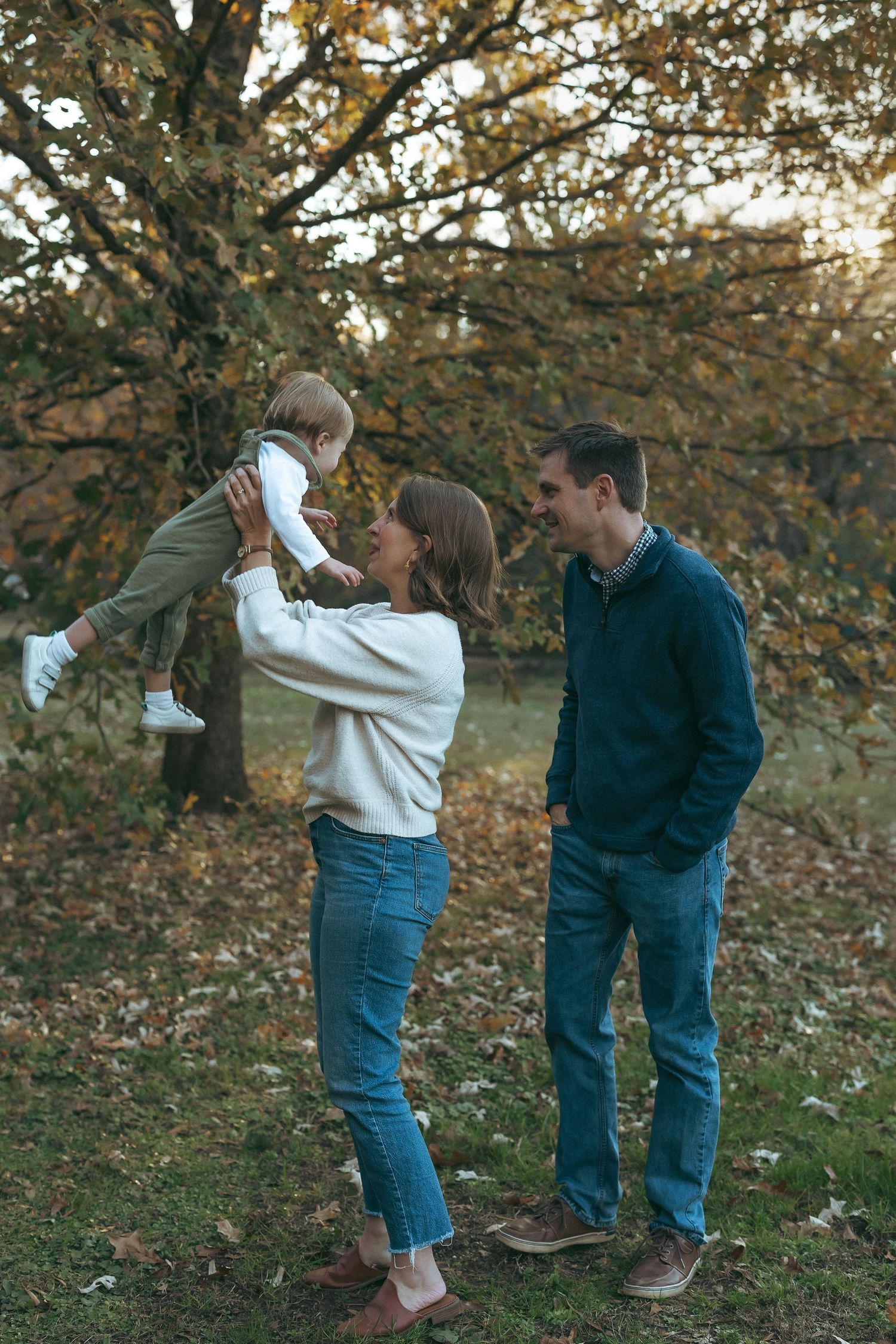 A family enjoys a tender autumn moment together outdoors with fall foliage in the background.