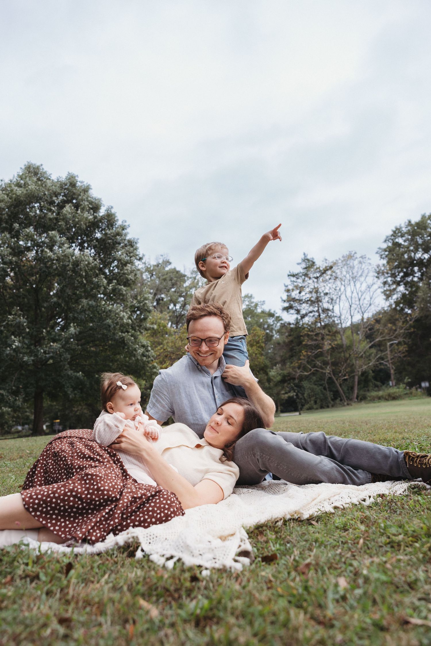 A family relaxes together on a blanket in a grassy park on an autumn day.