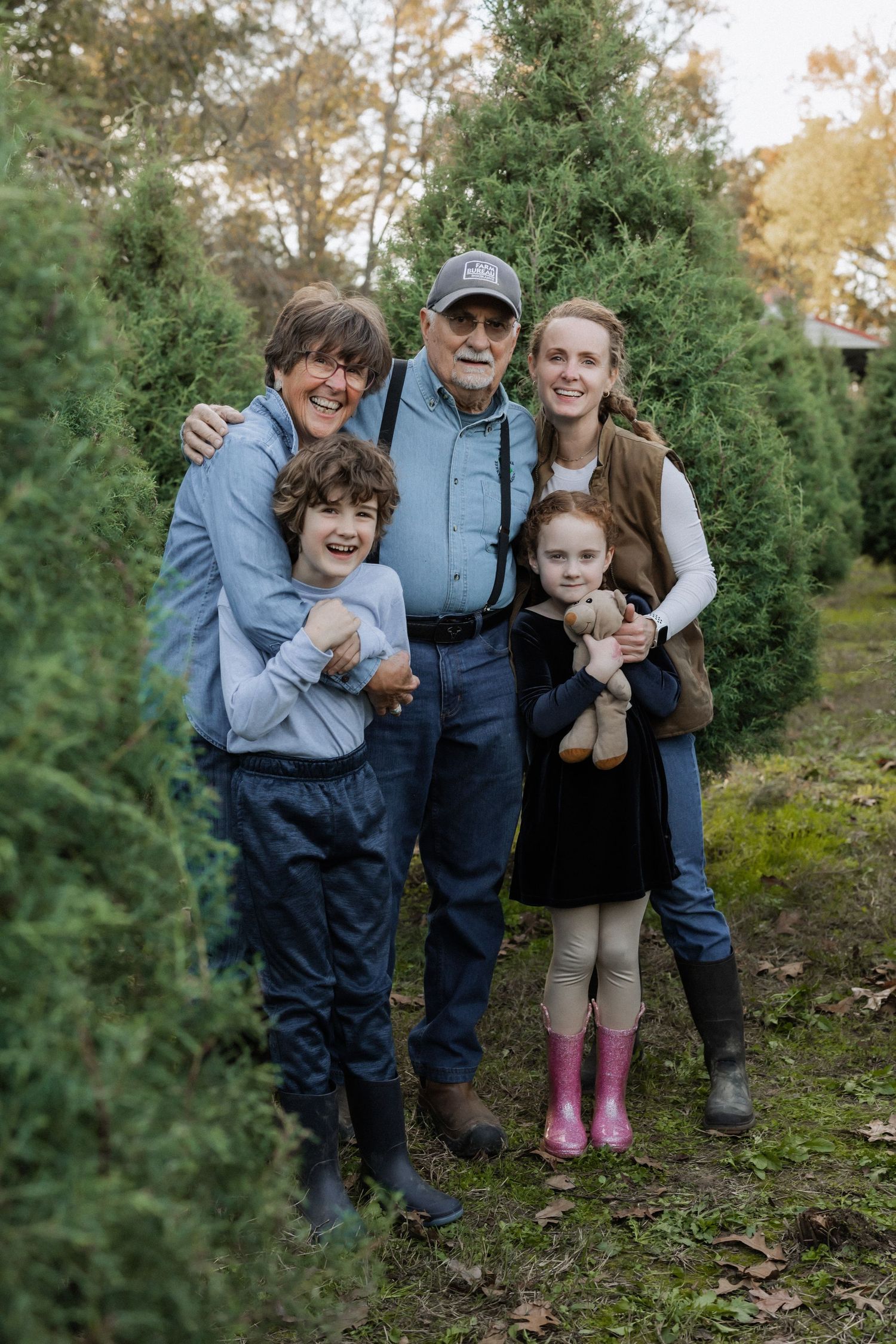A multi-generational family poses together outdoors among evergreen trees on a crisp autumn day.