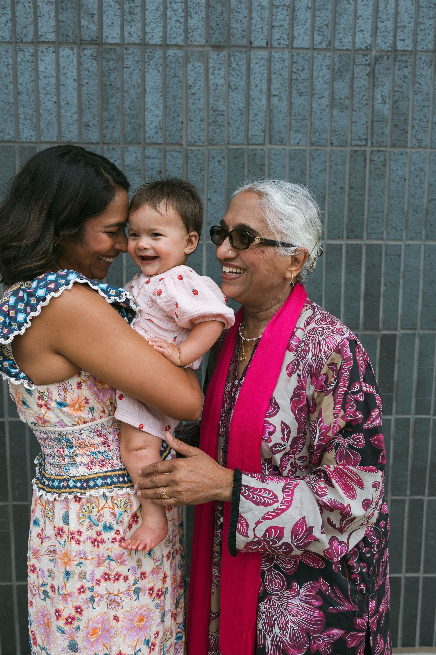 Three generations of women smiling together, grandmother in floral kimono, mother in sundress holding laughing baby girl.