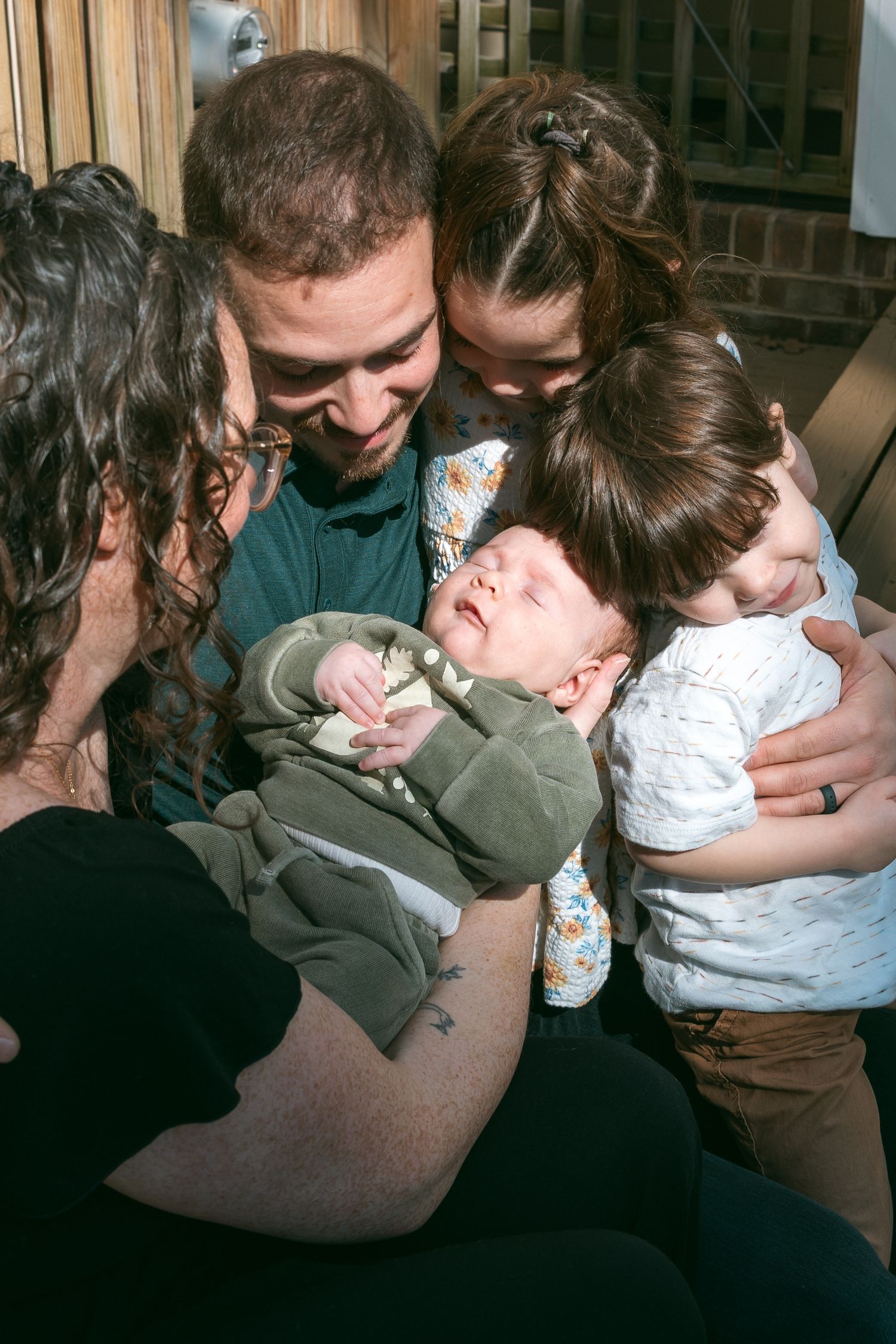 Family gathered closely admiring a sleeping newborn baby wrapped in a green blanket, sharing a tender moment together.