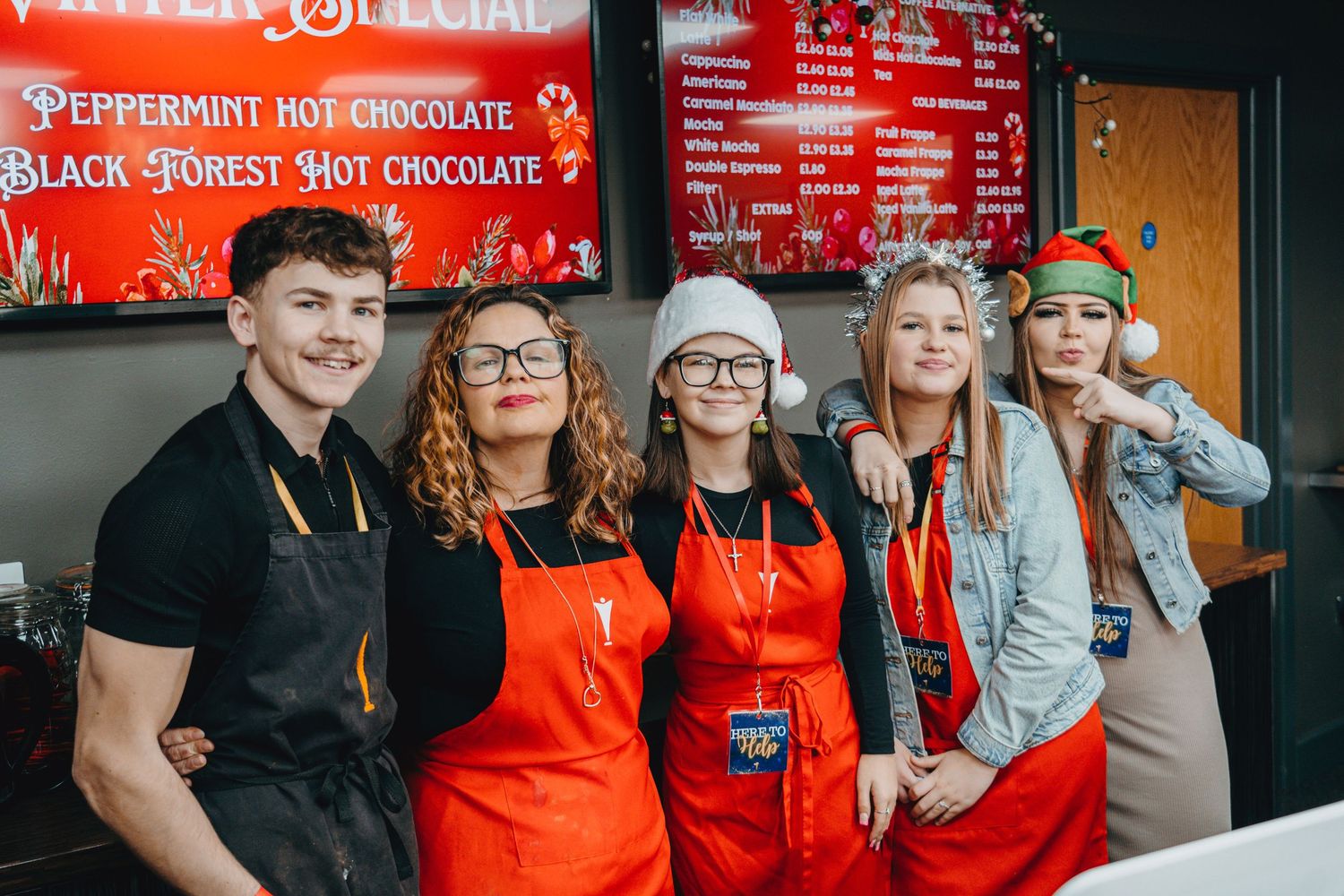 Staff members in red aprons pose together at chocolate shop counter.
