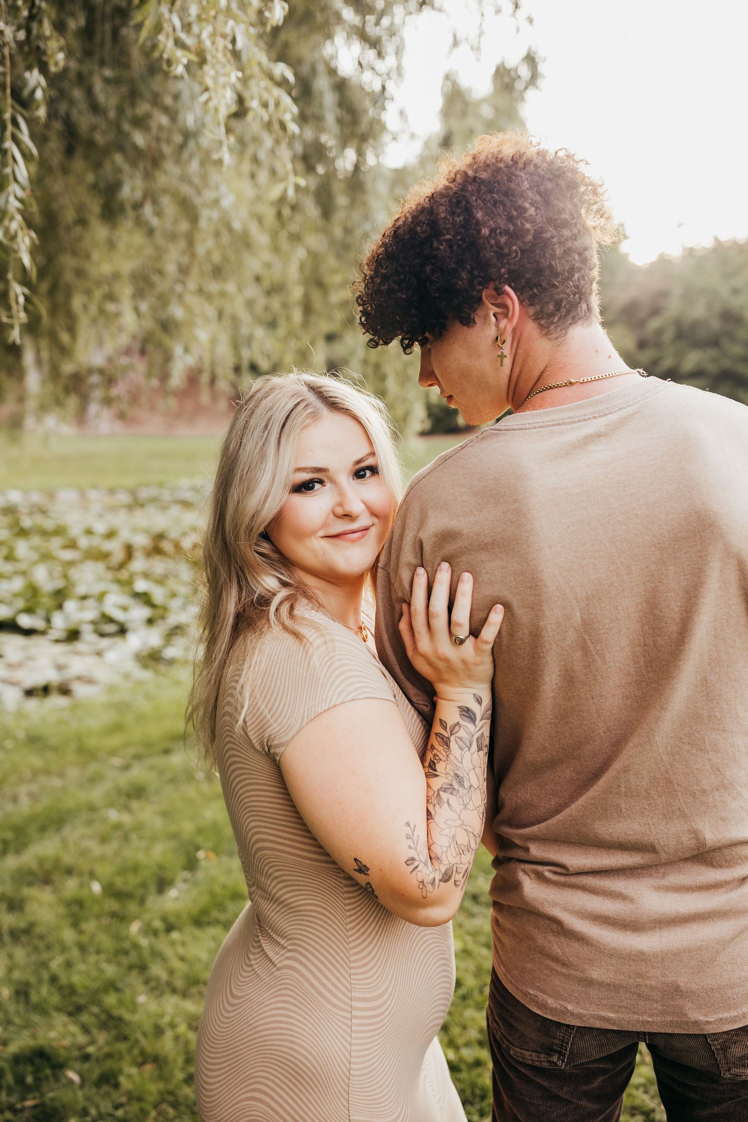 Romantic couple in matching beige outfits pose for an outdoor portrait in front of lush greenery.