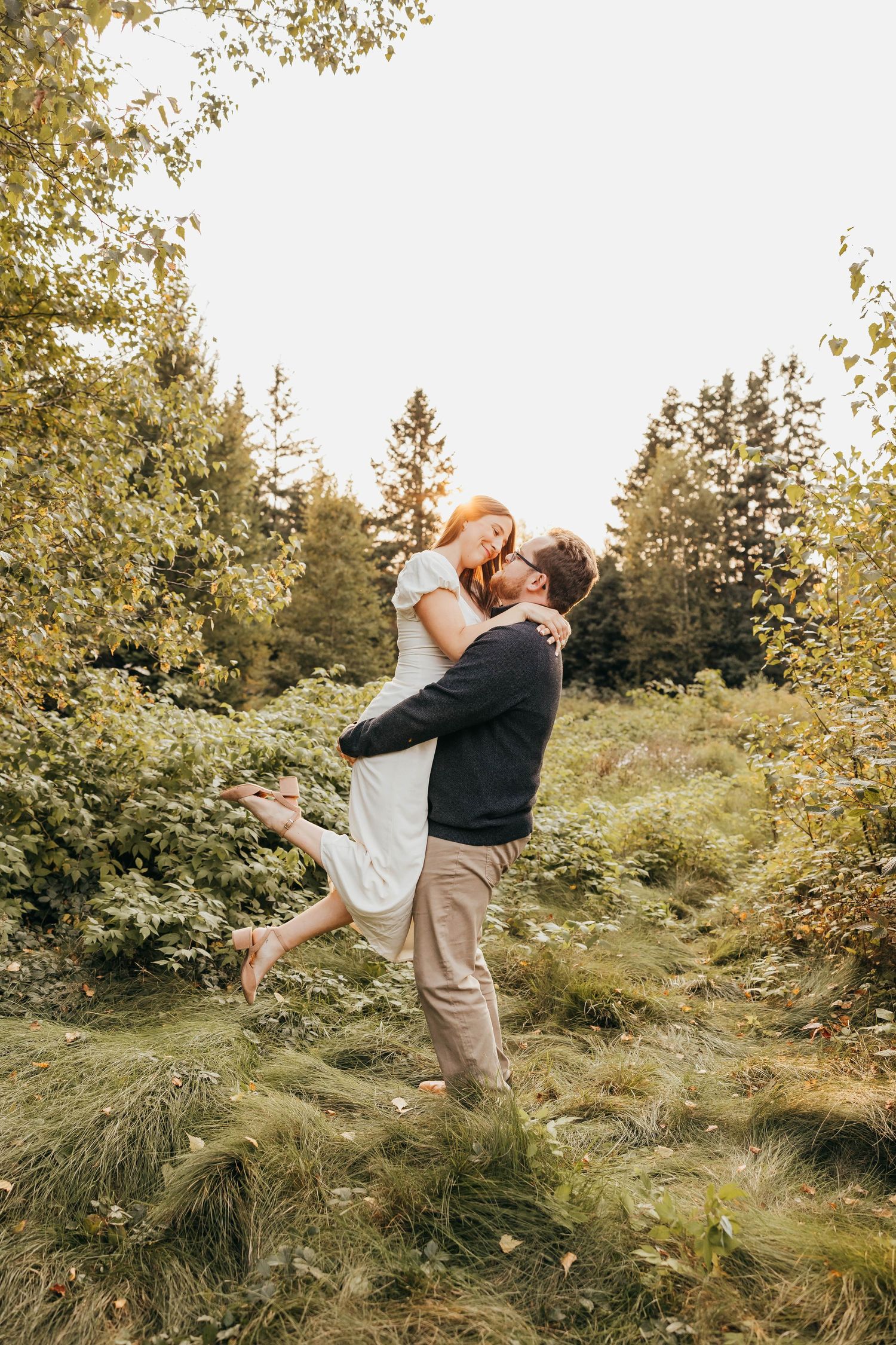 Joyful lift pose among trees in outdoor engagement session.