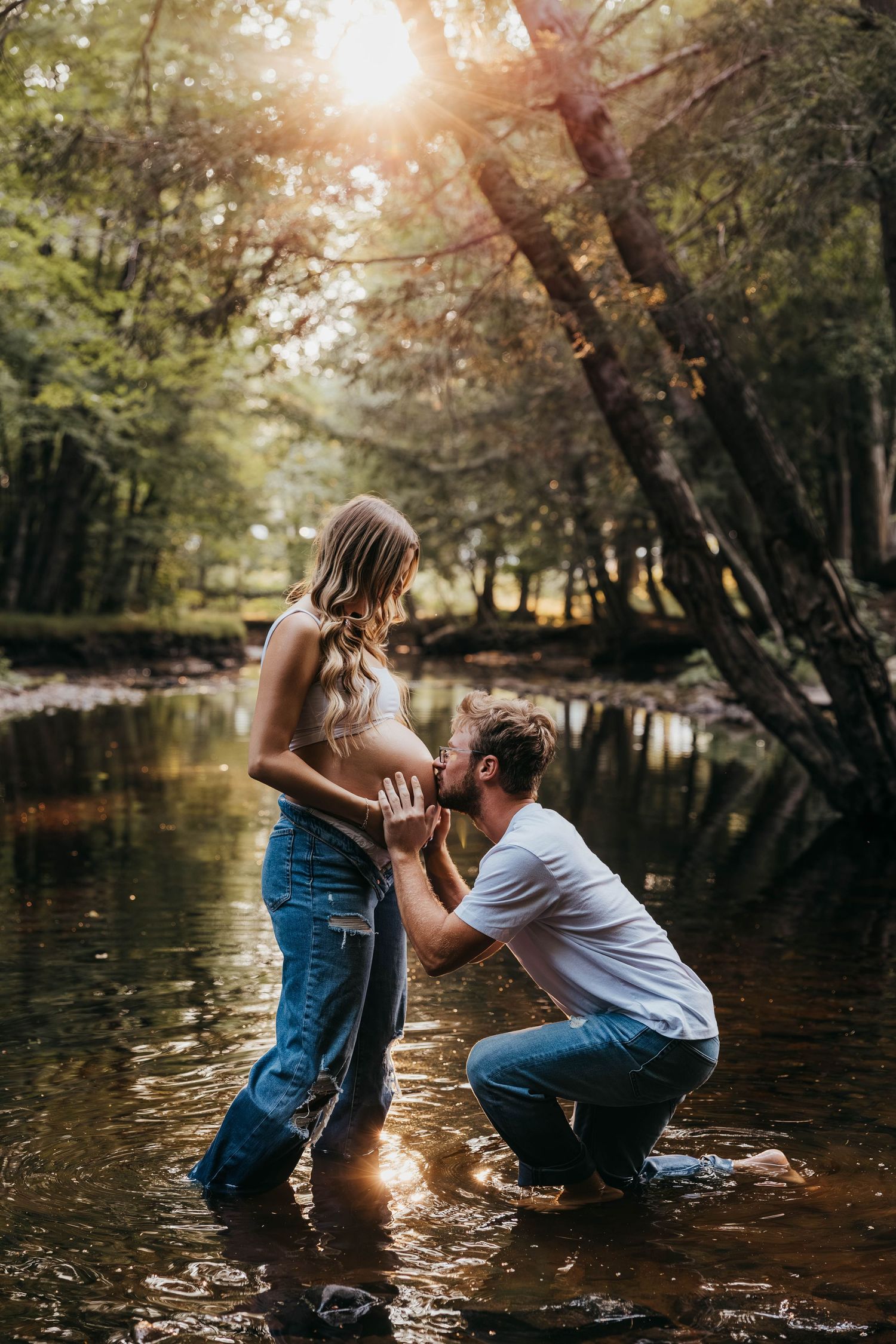 A romantic proposal moment captured in a sunlit creek with trees creating a magical forest backdrop.