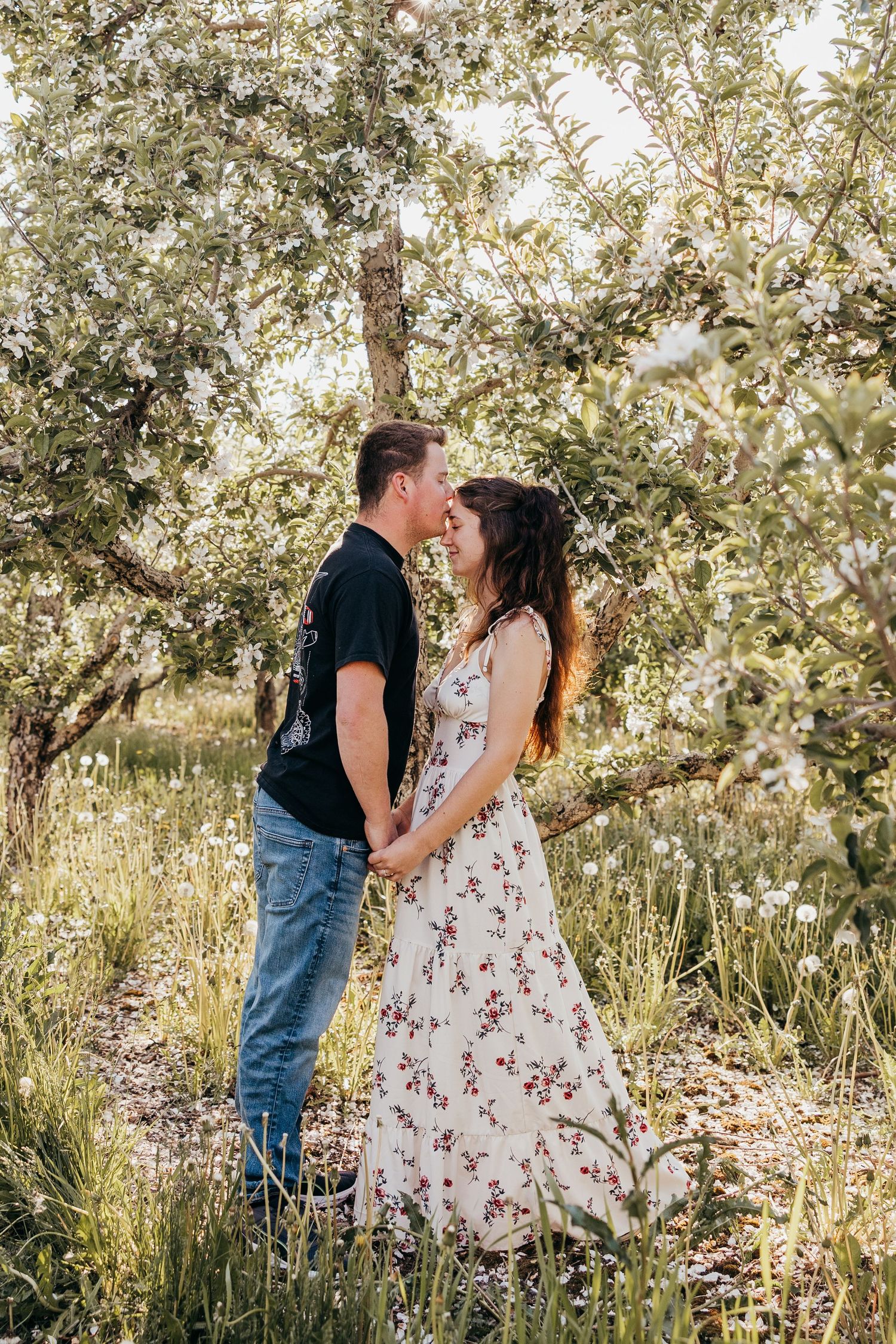 Couple sharing a romantic moment holding hands in a blooming orchard surrounded by wildflowers and lush greenery.