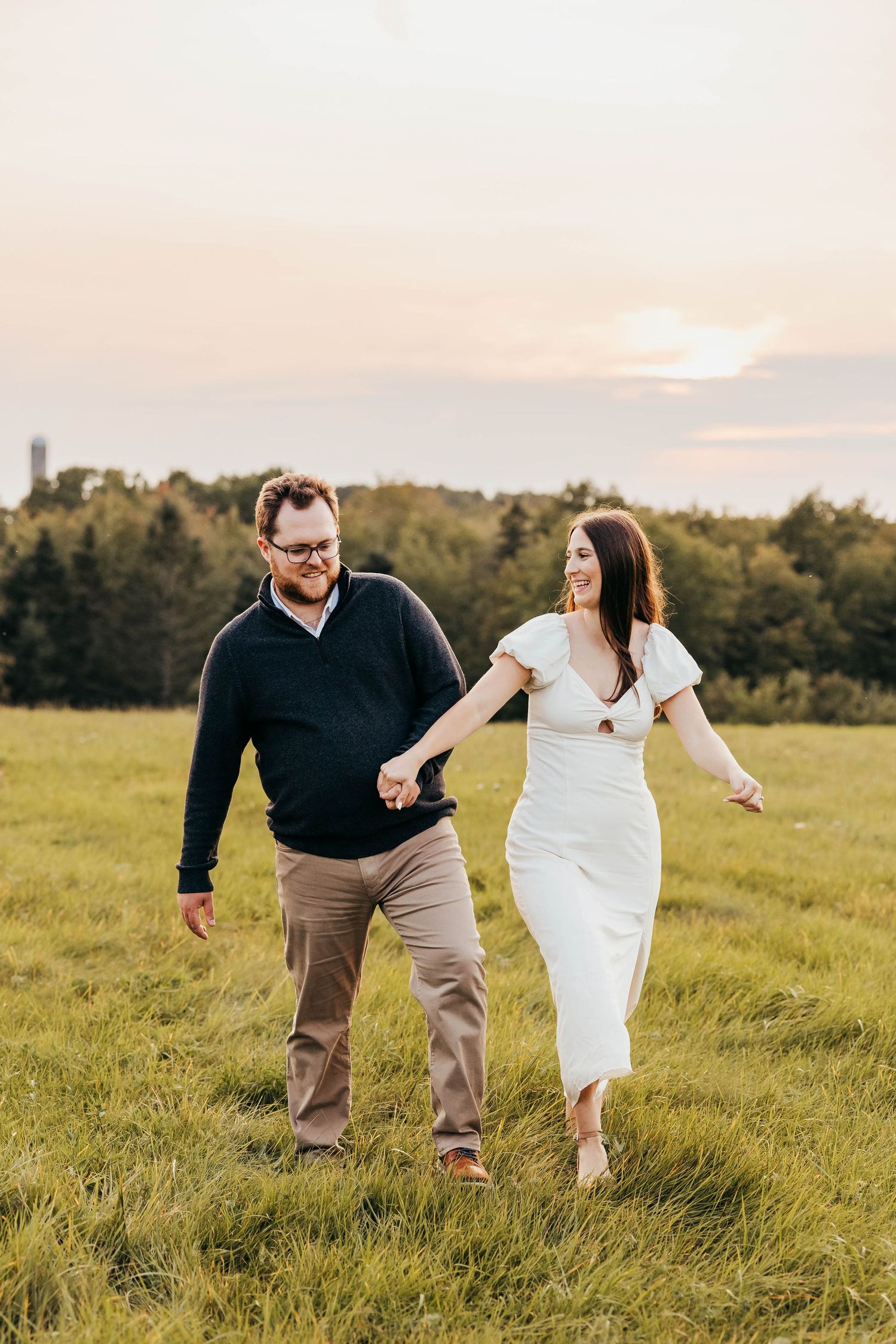 A couple walks hand in hand through a sunny meadow at golden hour.