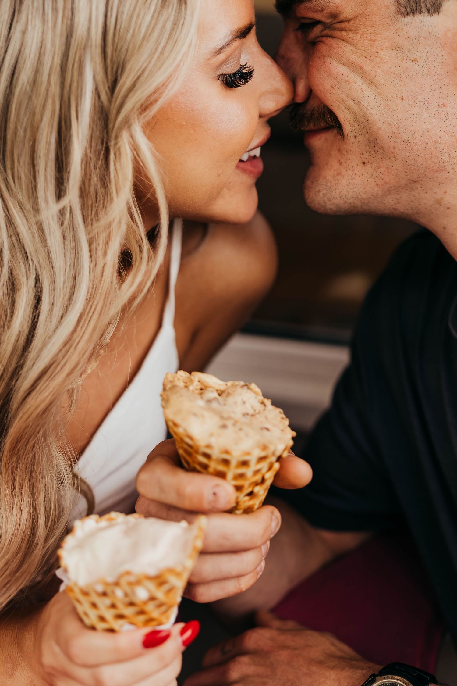 Couple sharing ice cream cones in an intimate romantic moment with blonde hair and red nails.