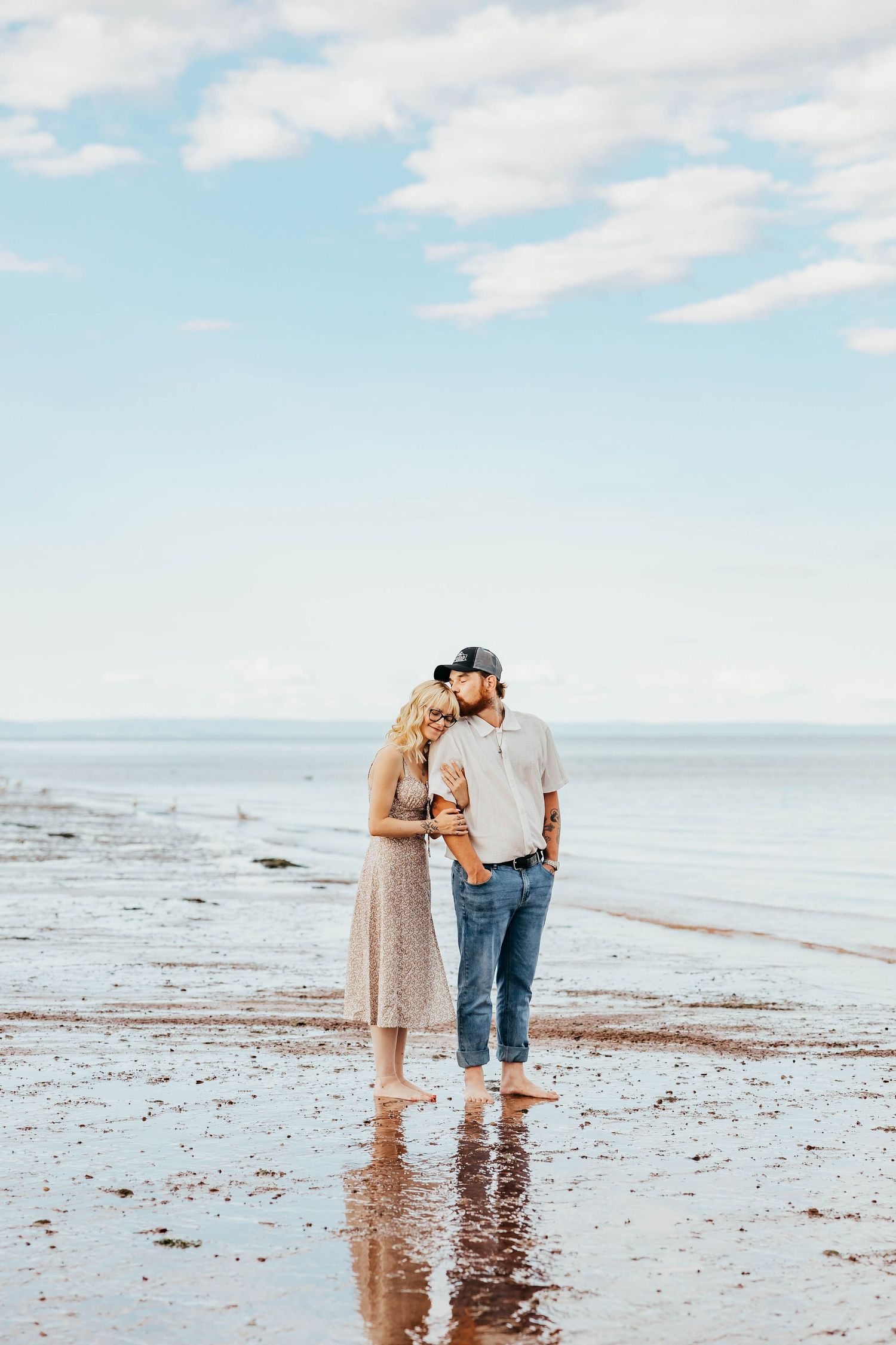 Couple sharing intimate moment on wet beach at sunset with ocean backdrop.