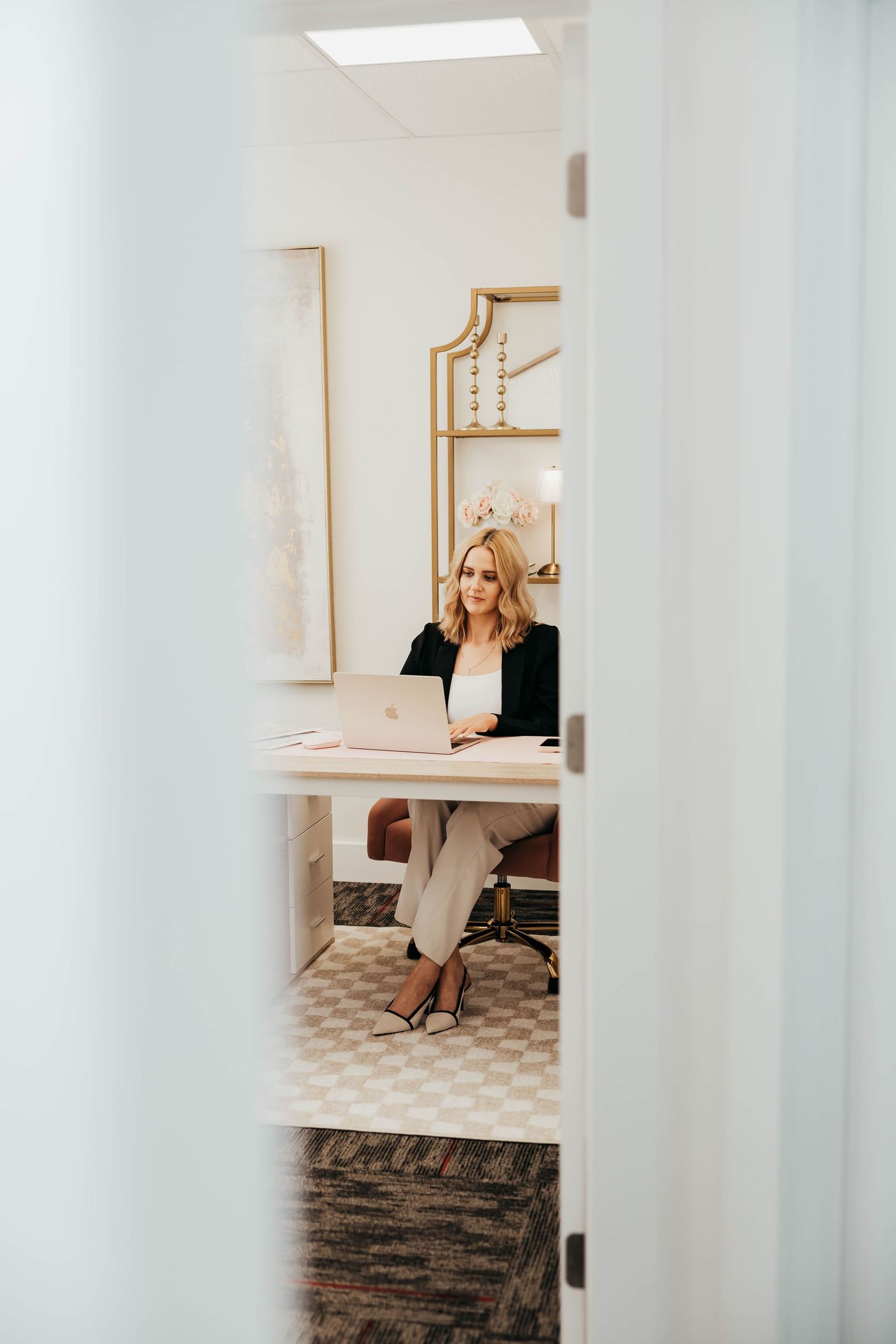 View through doorway of someone sitting at desk in bright modern office with patterned tile floor and gold accents.