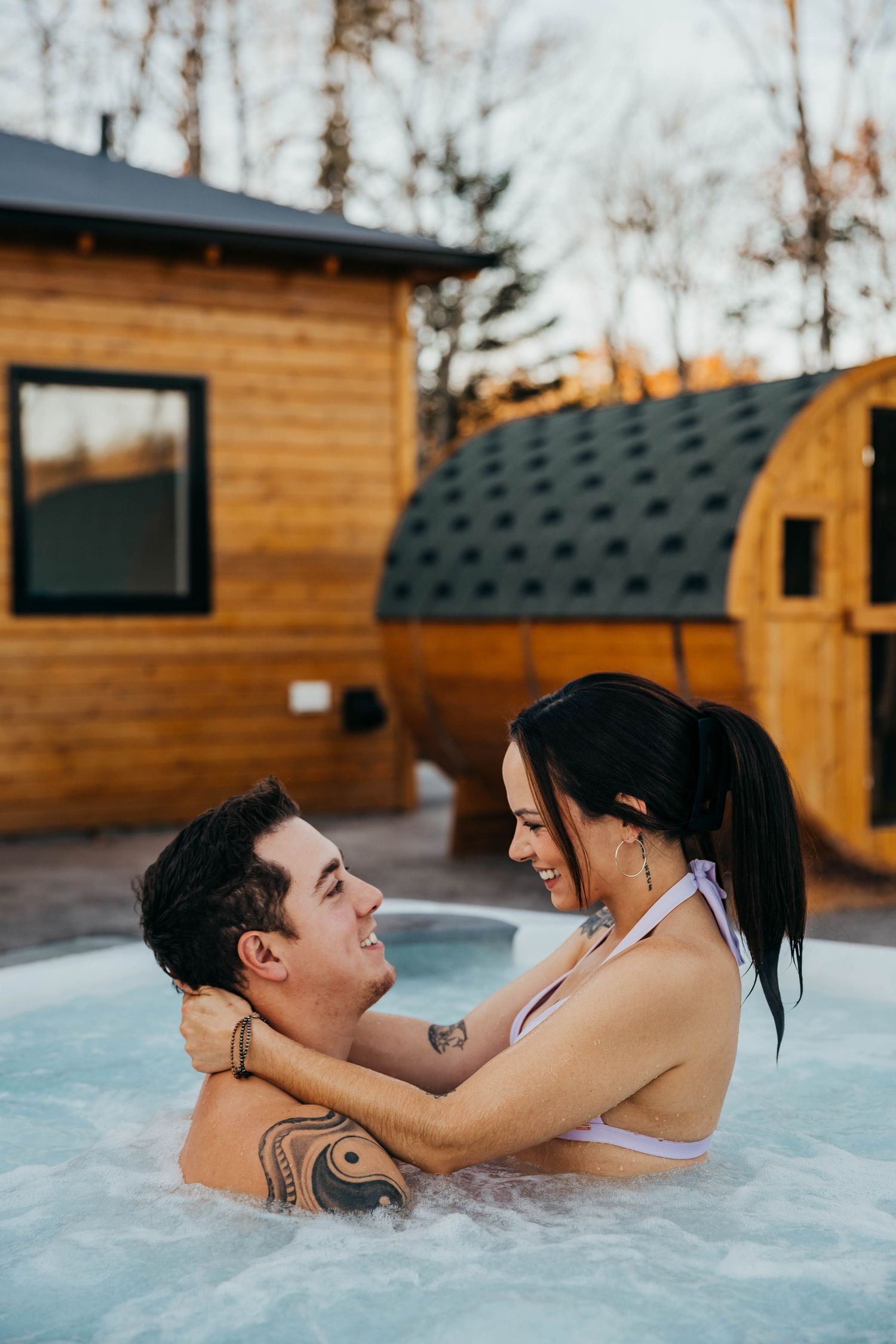Couple sharing romantic moment in hot tub outside rustic cabin.