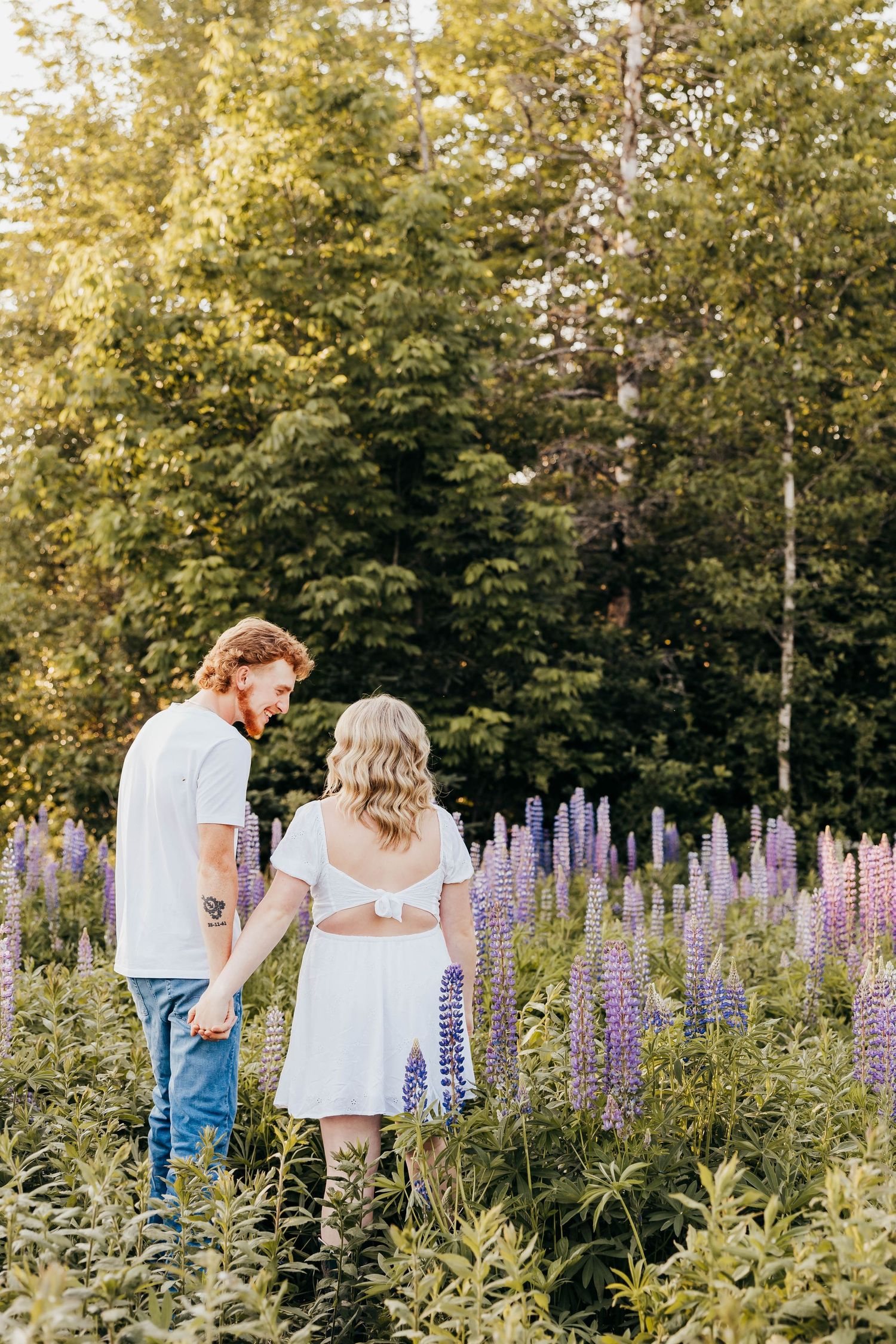 Couple standing in beautiful garden with blooming purple lupine flowers.