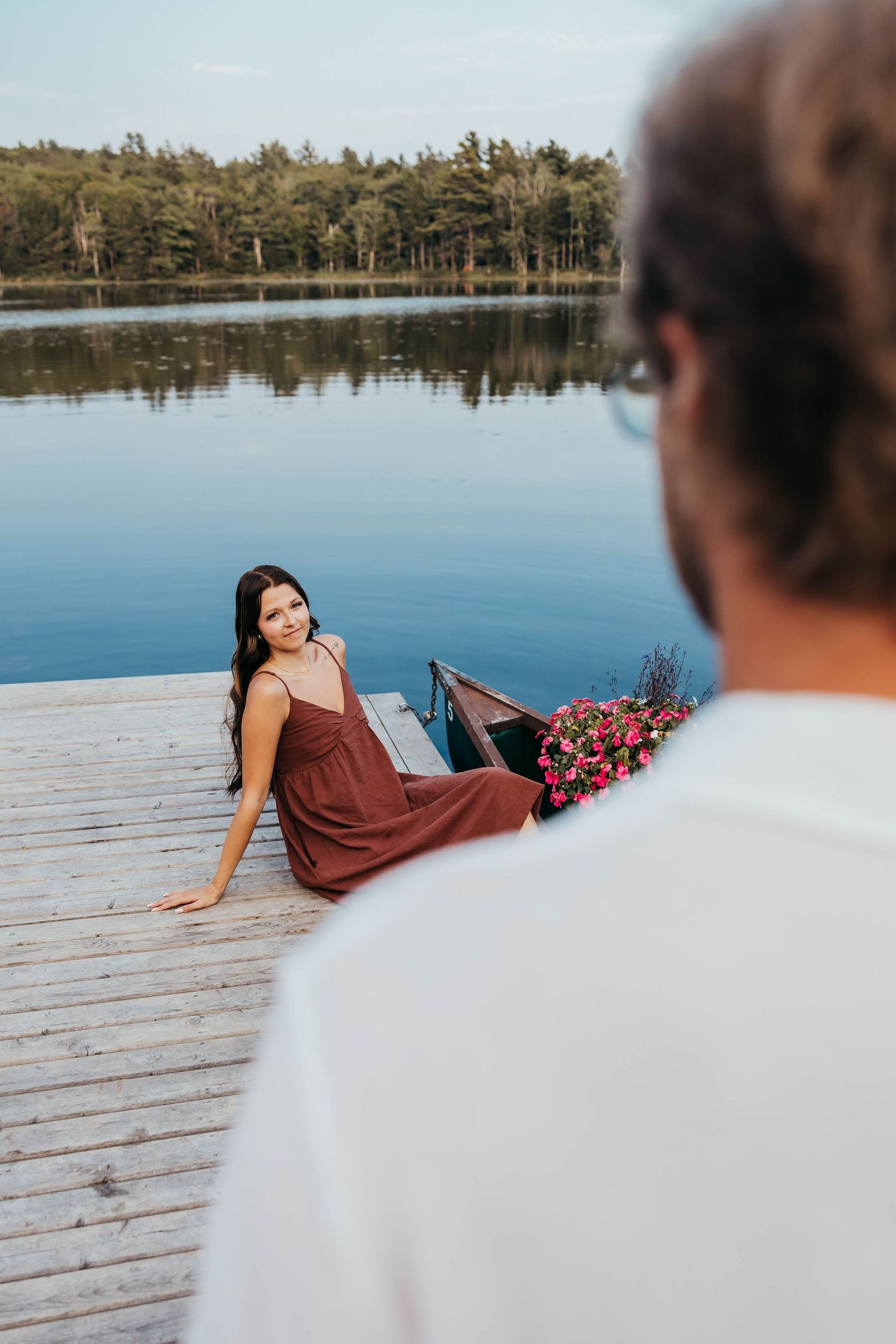 Romantic photoshoot on a wooden dock by a serene lake with pine trees in background.