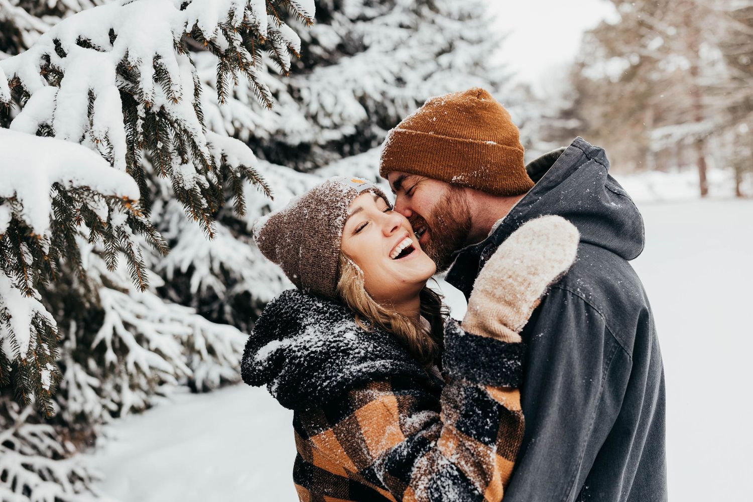 Playful winter couple moment in snowy forest wearing cozy winter attire.