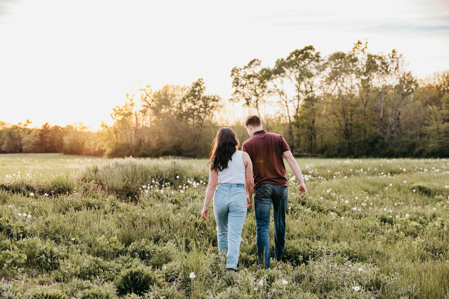 Couple walking hand in hand through a sunlit meadow at golden hour.