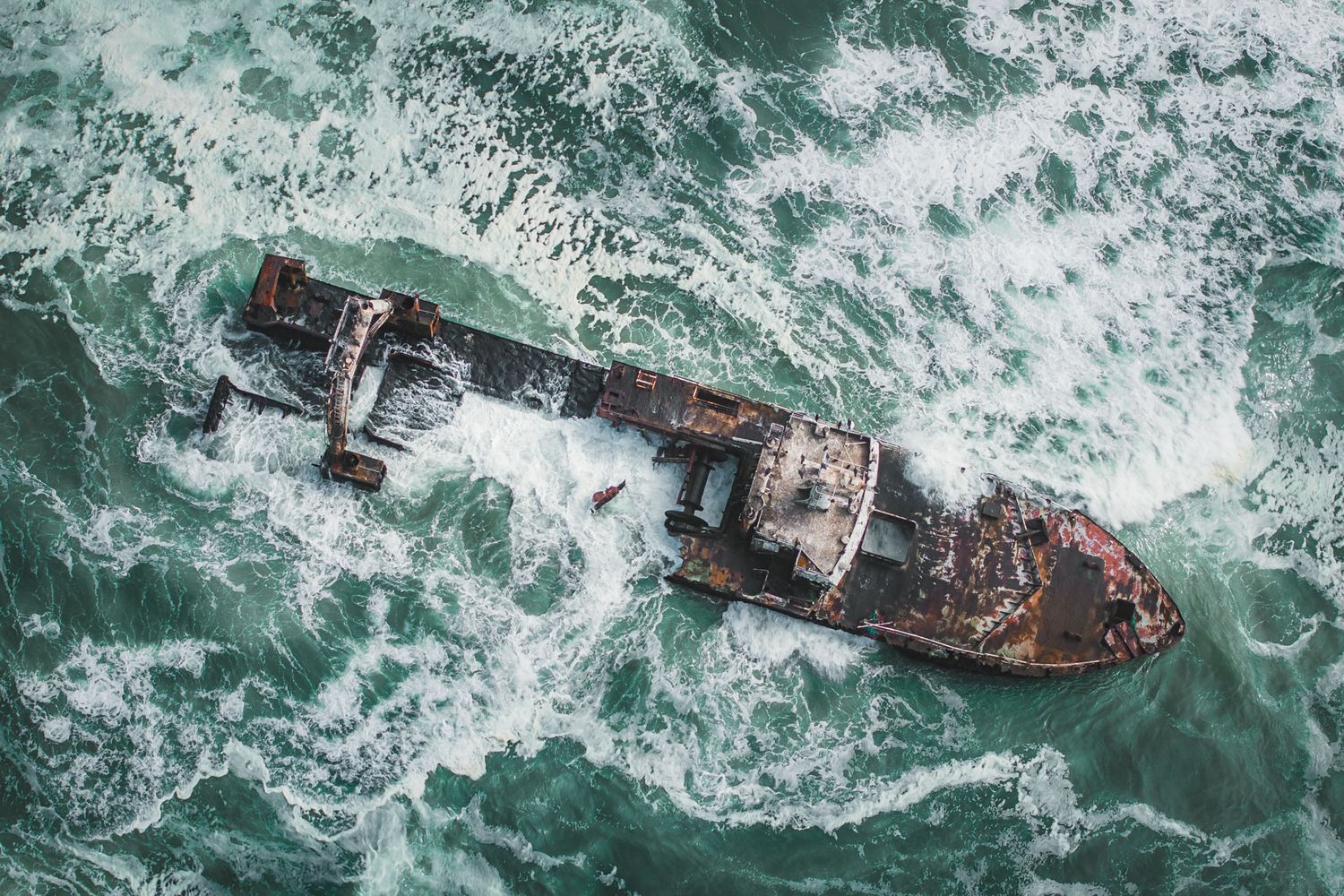 Aerial view of a shipwreck surrounded by turquoise churning ocean waters.