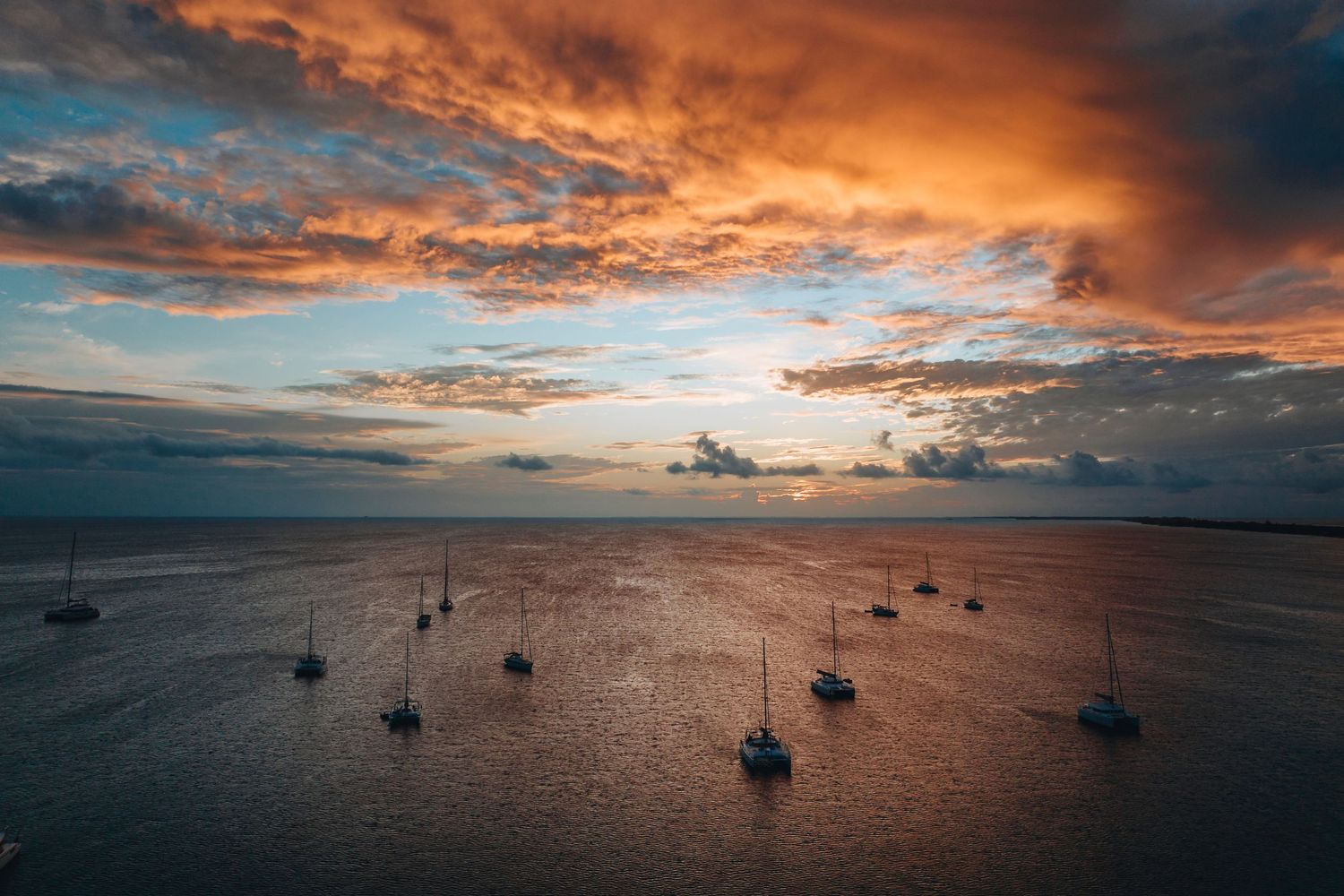 Dramatic orange sunset over a harbor filled with anchored sailboats.