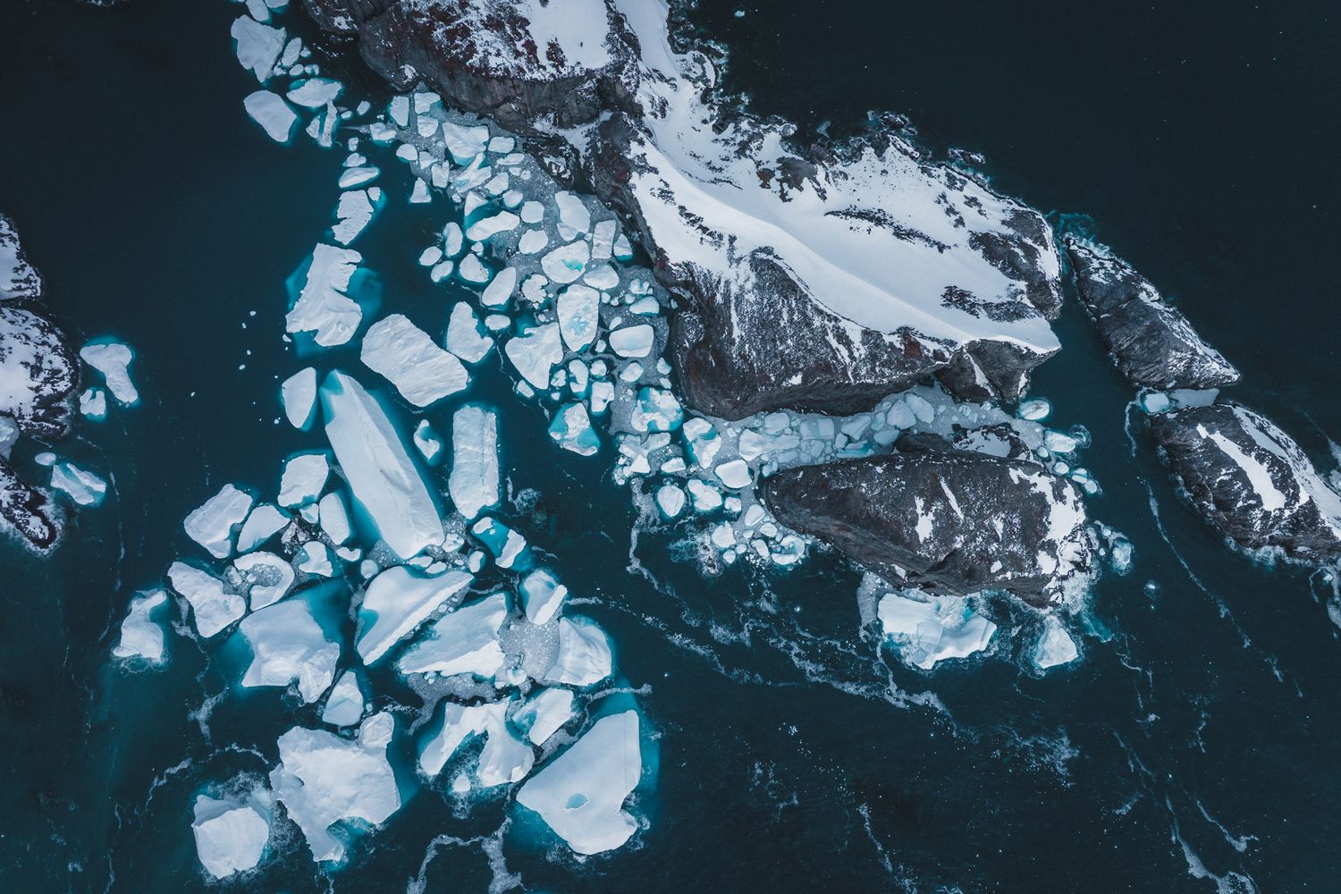 Aerial view of fractured ice floes and glacial formations floating in dark ocean waters.