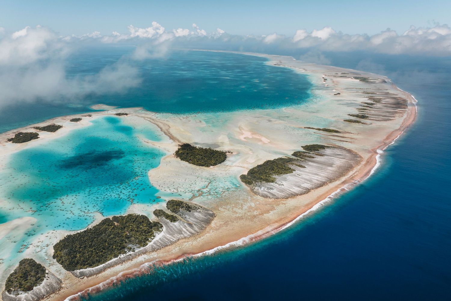 Bird's eye view of a tropical atoll with curved sandy beaches and turquoise lagoons in the Pacific Ocean.